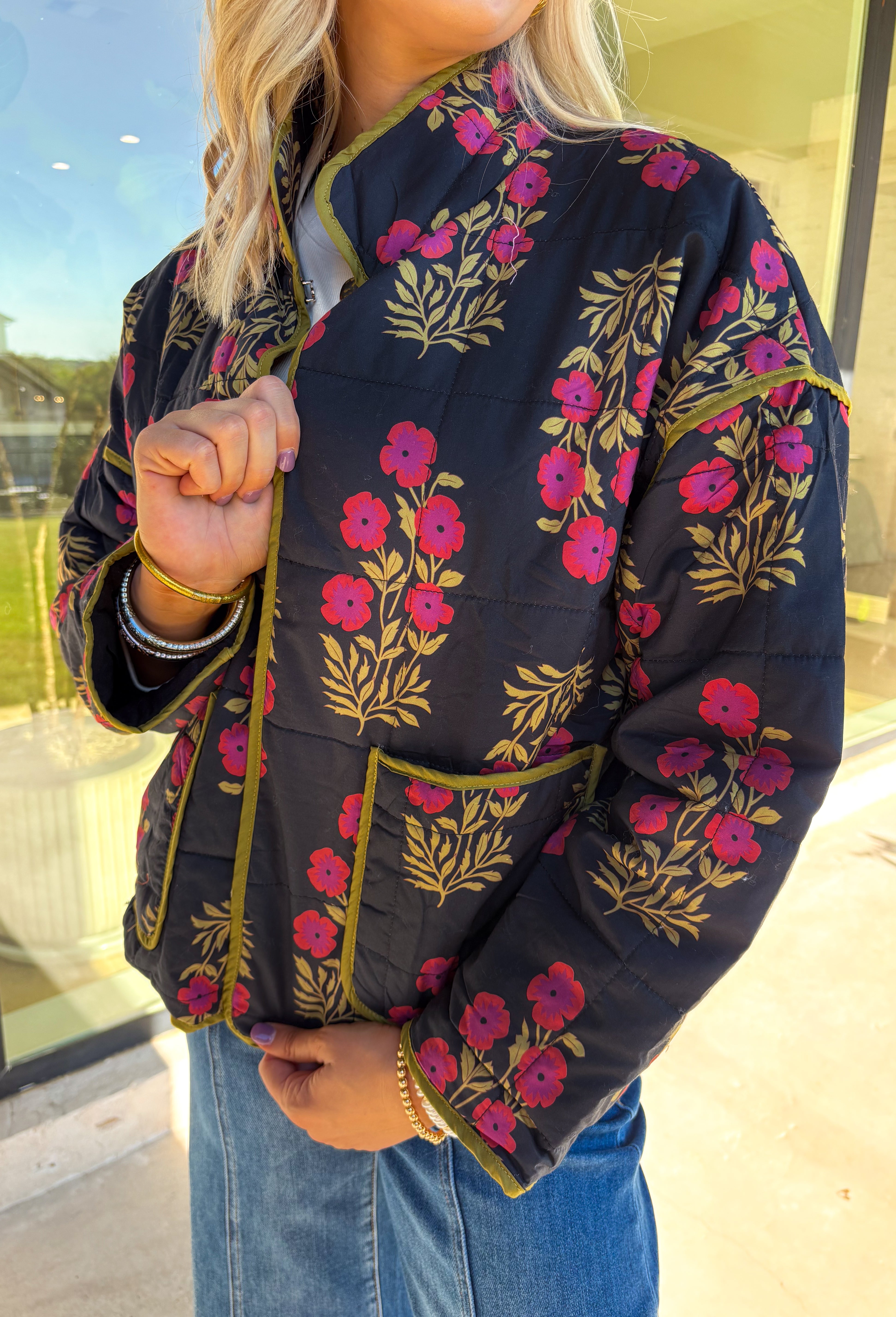 Wrap up in seasonal style with this black quilted jacket featuring a rich botanical print in olive and burgundy tones. Contrast binding highlights the edges for a polished finish, while front patch pockets add both function and charm. The hook-and-eye closure keeps the silhouette clean and simple, and the all-cotton design makes it cozy yet breathable for cool fall days. Whether layered over a sweater or paired with a casual tee, this jacket is a statement piece you’ll wear on repeat.