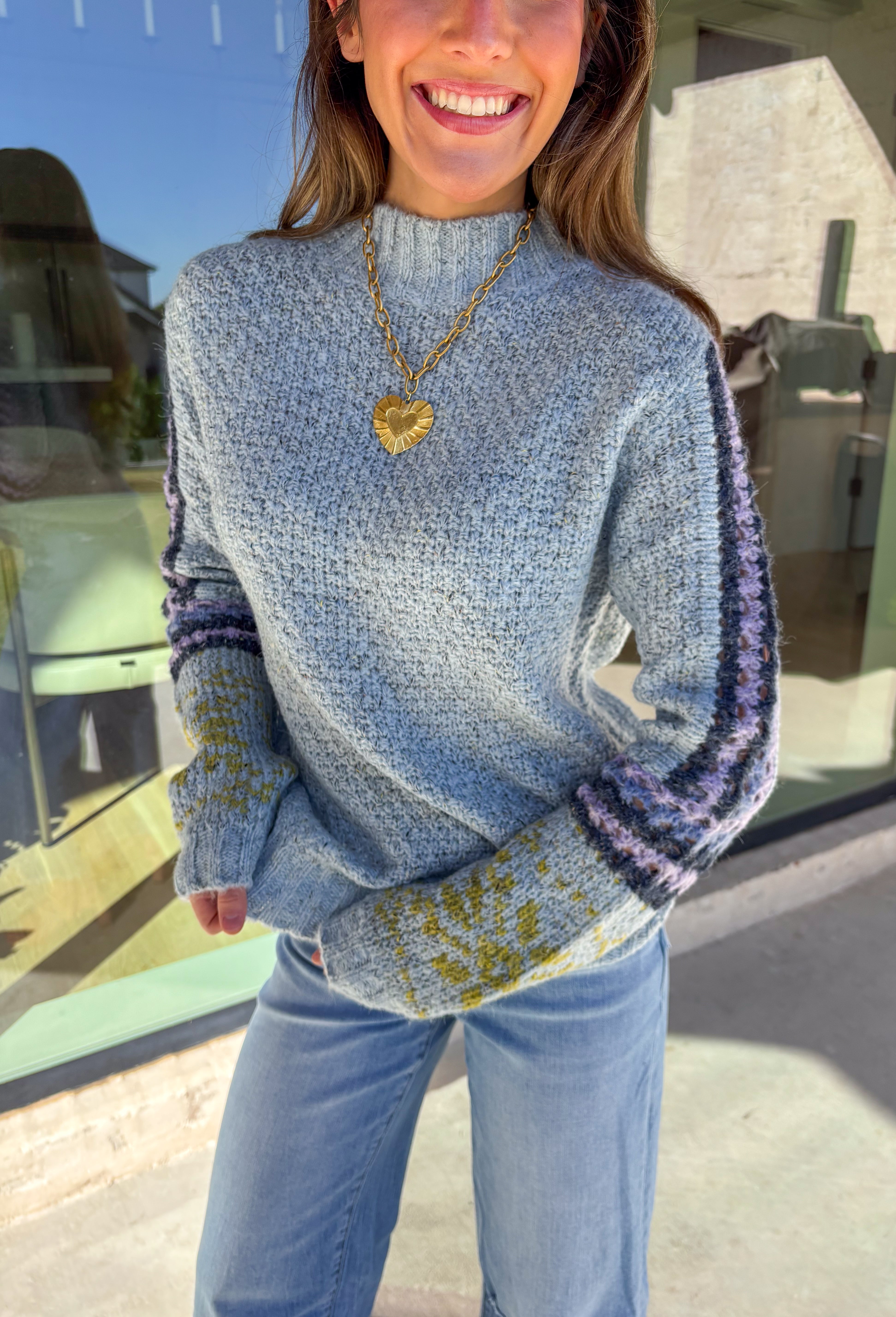 Bring a little color to chilly days with this cozy light blue knit sweater by Mystree. The mock neck design keeps you warm, while the abstract print sleeves—featuring shades of navy, light purple, and green—add a playful, modern twist. Soft, warm, and stylish, this sweater is an easy pick for staying cozy and cute all season long.