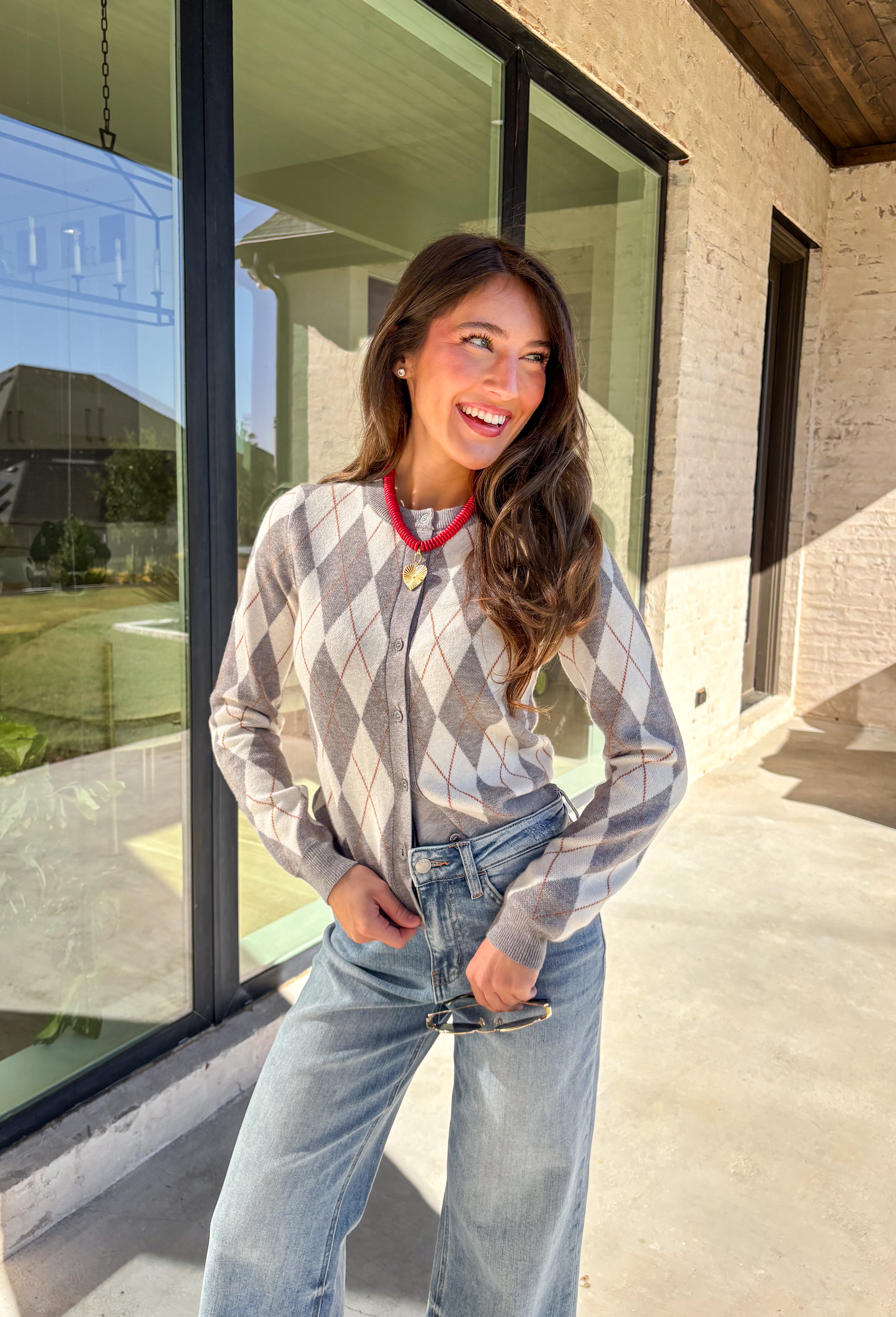 Classic pattern, cozy feel—this button-down cardigan by Haute Monde is the perfect layering piece for the season. Featuring a timeless gray and off-white argyle print with tan accents, it’s a modern twist on a preppy staple. The button-front design and soft knit fabric make it an easy go-to whether you’re dressing up for work or keeping it casual on weekends.