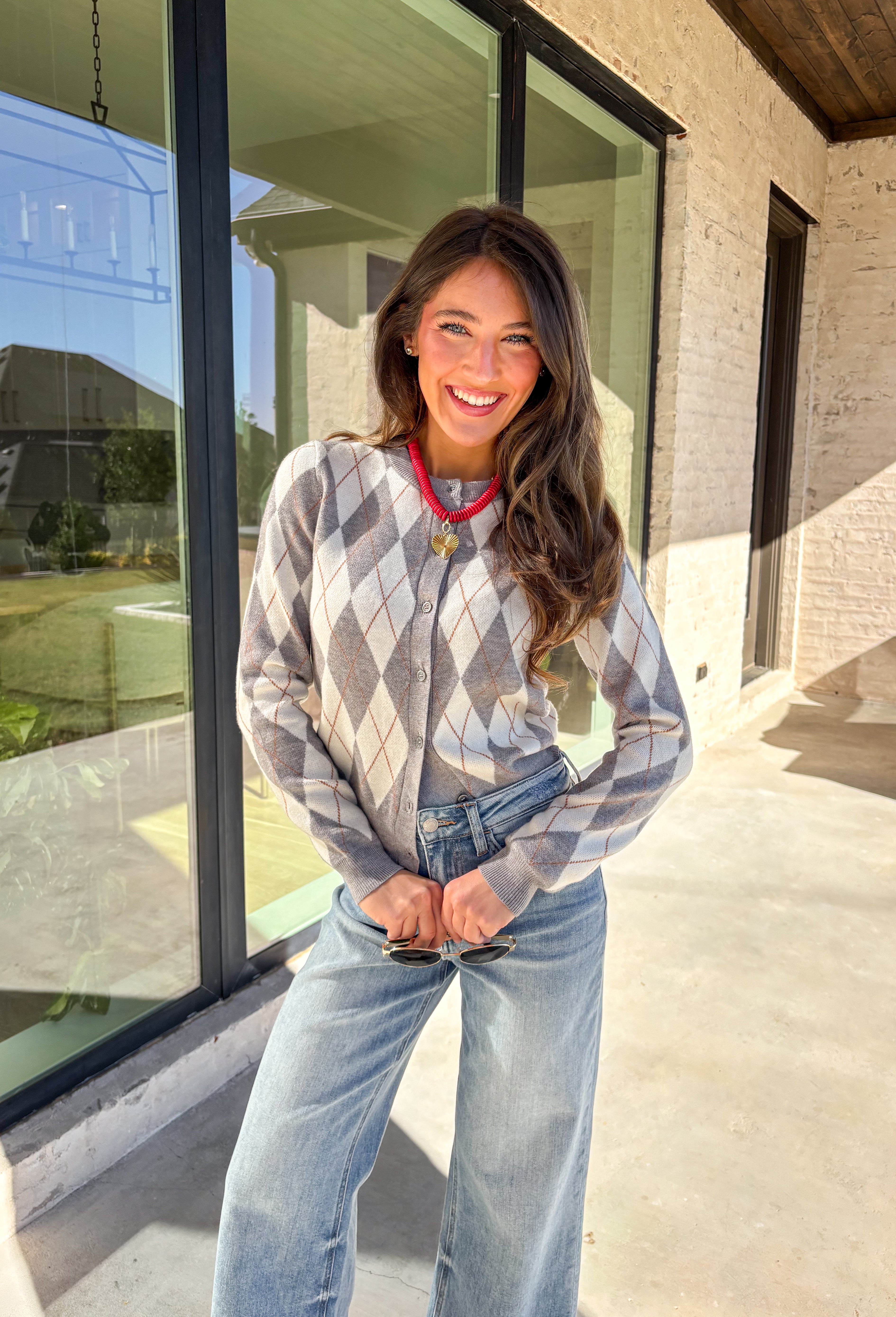 Classic pattern, cozy feel—this button-down cardigan by Haute Monde is the perfect layering piece for the season. Featuring a timeless gray and off-white argyle print with tan accents, it’s a modern twist on a preppy staple. The button-front design and soft knit fabric make it an easy go-to whether you’re dressing up for work or keeping it casual on weekends.