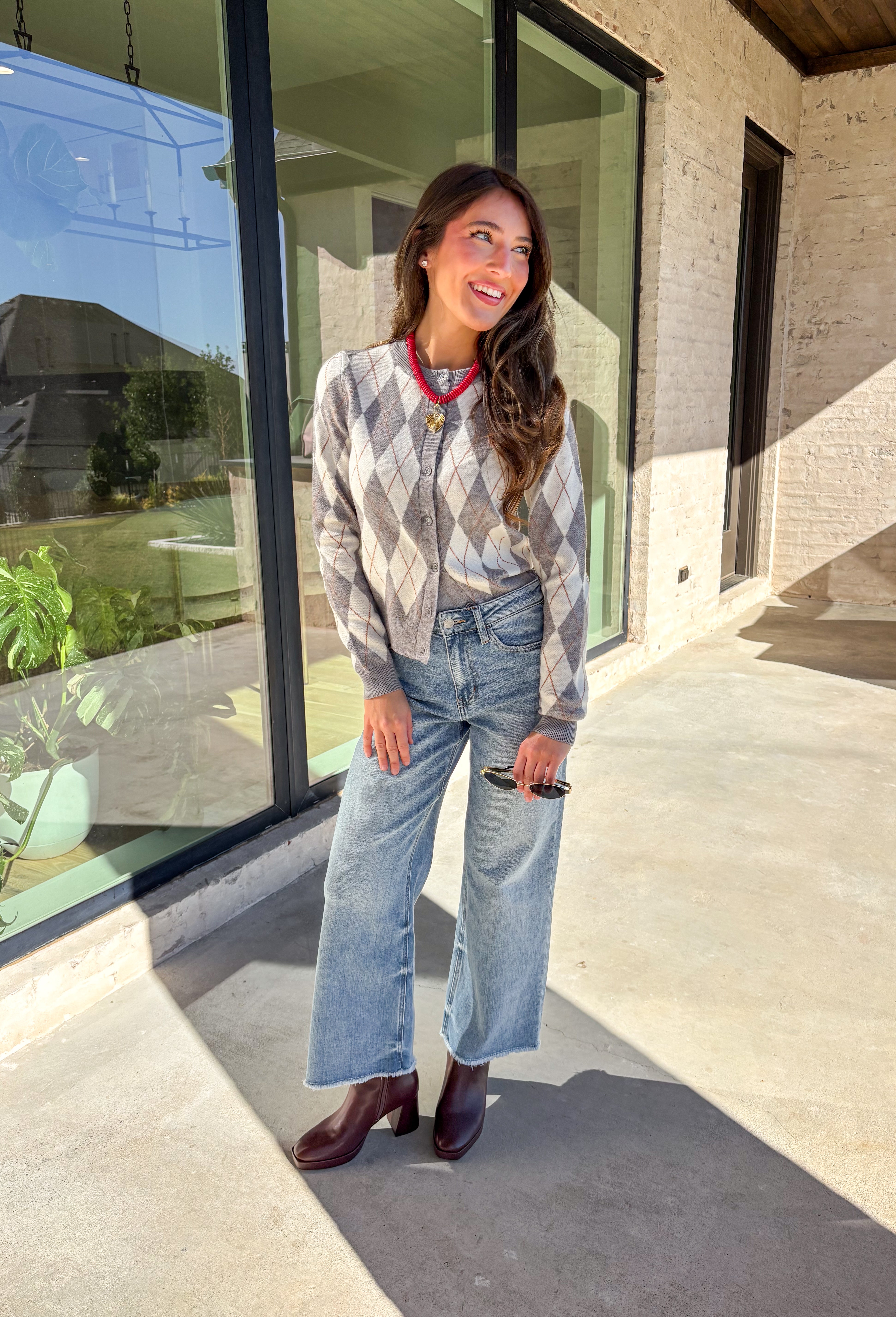 Classic pattern, cozy feel—this button-down cardigan by Haute Monde is the perfect layering piece for the season. Featuring a timeless gray and off-white argyle print with tan accents, it’s a modern twist on a preppy staple. The button-front design and soft knit fabric make it an easy go-to whether you’re dressing up for work or keeping it casual on weekends.