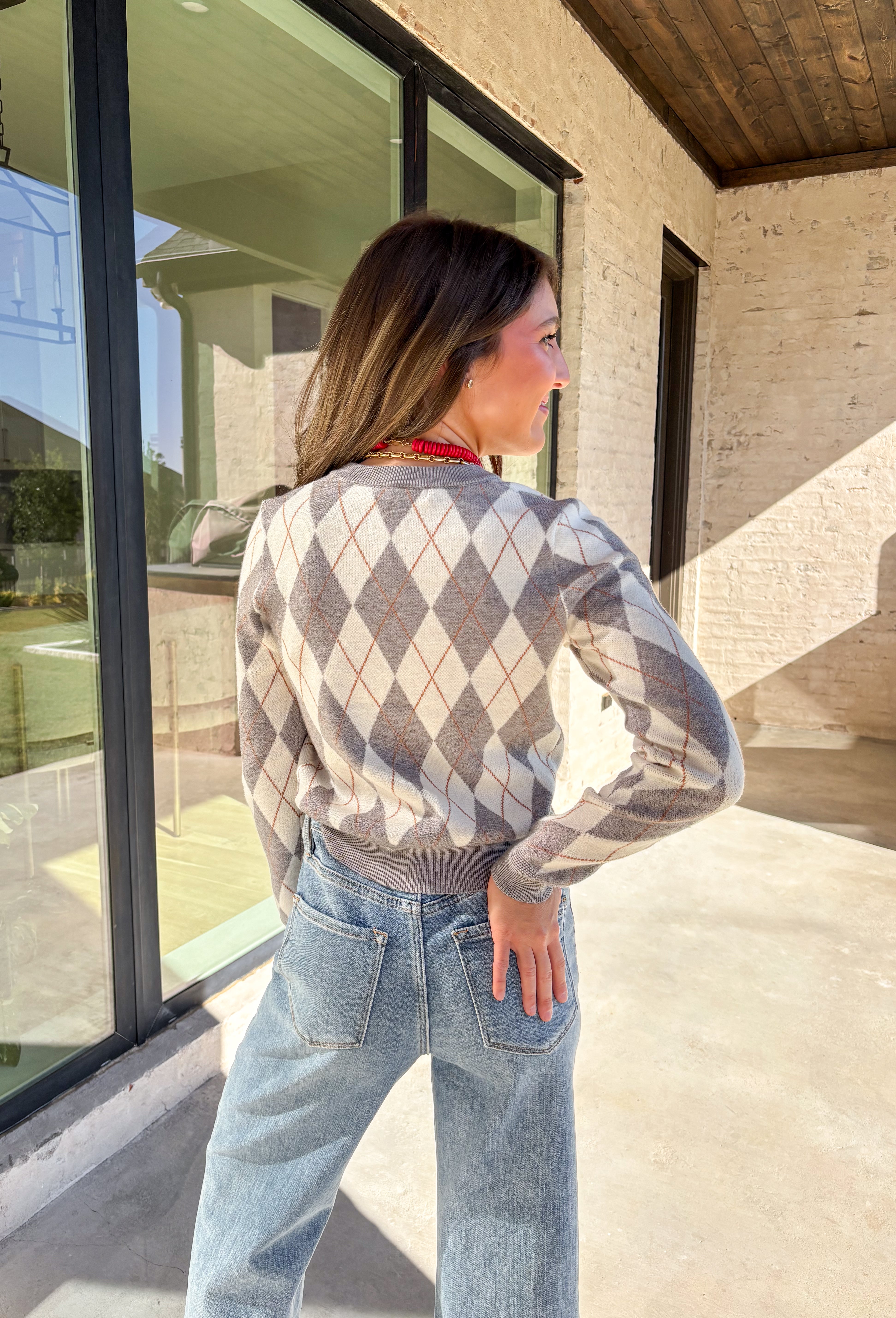 Classic pattern, cozy feel—this button-down cardigan by Haute Monde is the perfect layering piece for the season. Featuring a timeless gray and off-white argyle print with tan accents, it’s a modern twist on a preppy staple. The button-front design and soft knit fabric make it an easy go-to whether you’re dressing up for work or keeping it casual on weekends.