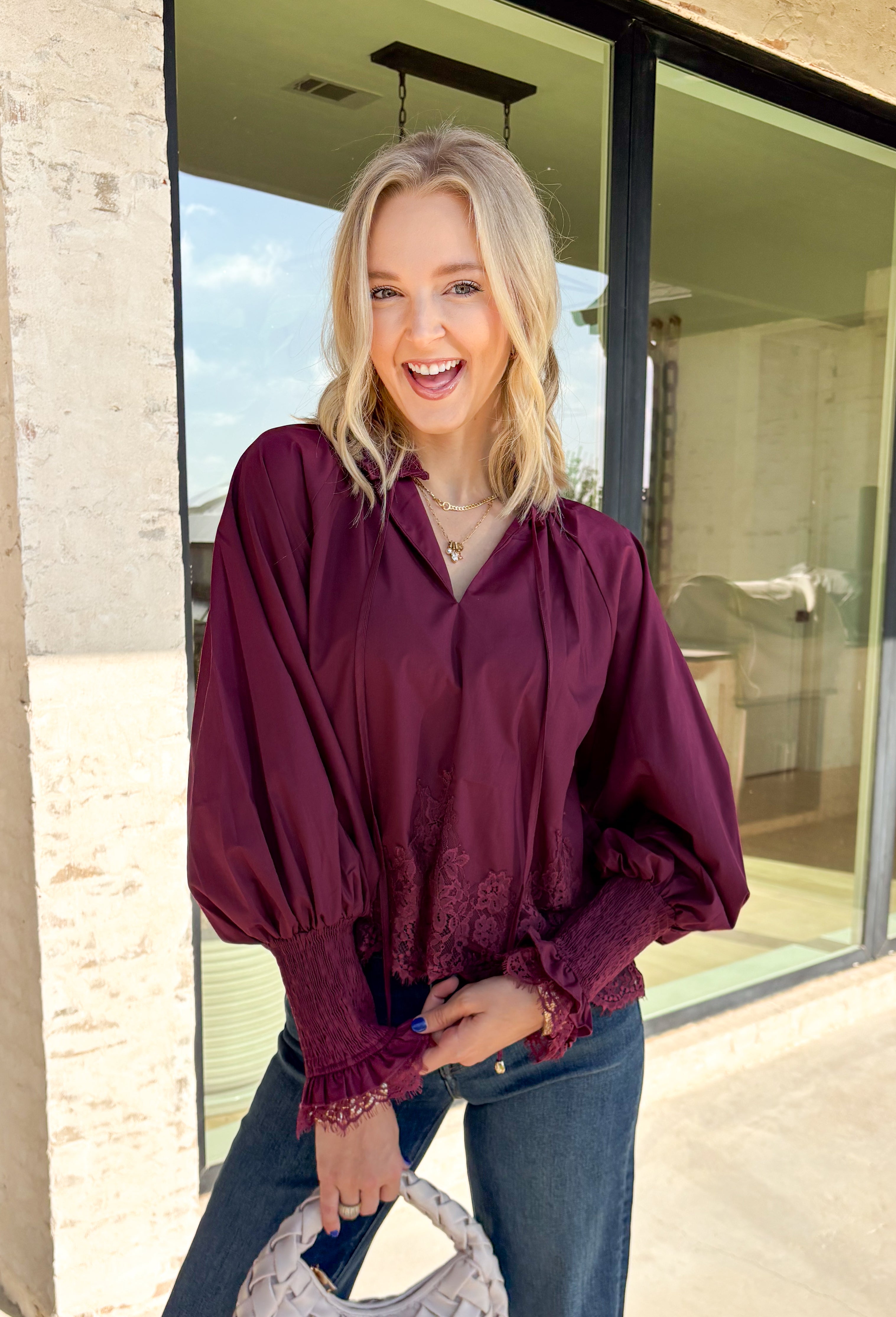 Bring a touch of romantic charm to your fall wardrobe with this beautifully detailed blouse from Entro. Designed in a rich burgundy hue, this feminine top features a softly smocked neckline with a delicate front tie for an effortlessly graceful look. The long sleeves are finished with smocked cuffs and lace trim, while the lace hem adds an elegant finishing touch. 