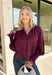 Bring a touch of romantic charm to your fall wardrobe with this beautifully detailed blouse from Entro. Designed in a rich burgundy hue, this feminine top features a softly smocked neckline with a delicate front tie for an effortlessly graceful look. The long sleeves are finished with smocked cuffs and lace trim, while the lace hem adds an elegant finishing touch. 