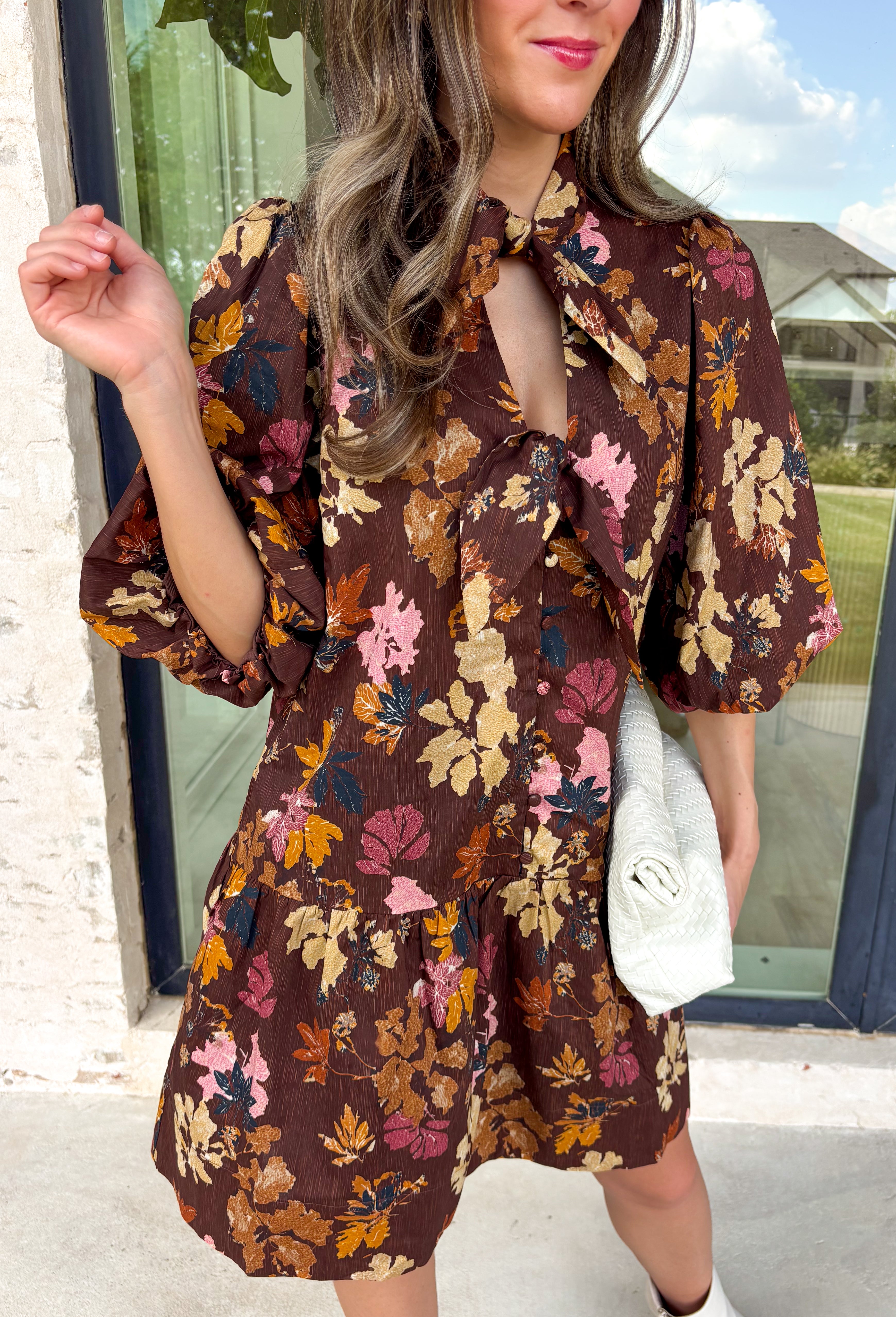 Capture the beauty of the season in this effortlessly feminine dress from Entro. Designed with a rich brown backdrop and a fall-inspired floral print with delicate leaf-like details, this charming dress is perfect for everything from brunch dates to seasonal celebrations. The flattering v-neckline features sweet tie details at the neck and bust, while decorative front buttons add timeless appeal. 