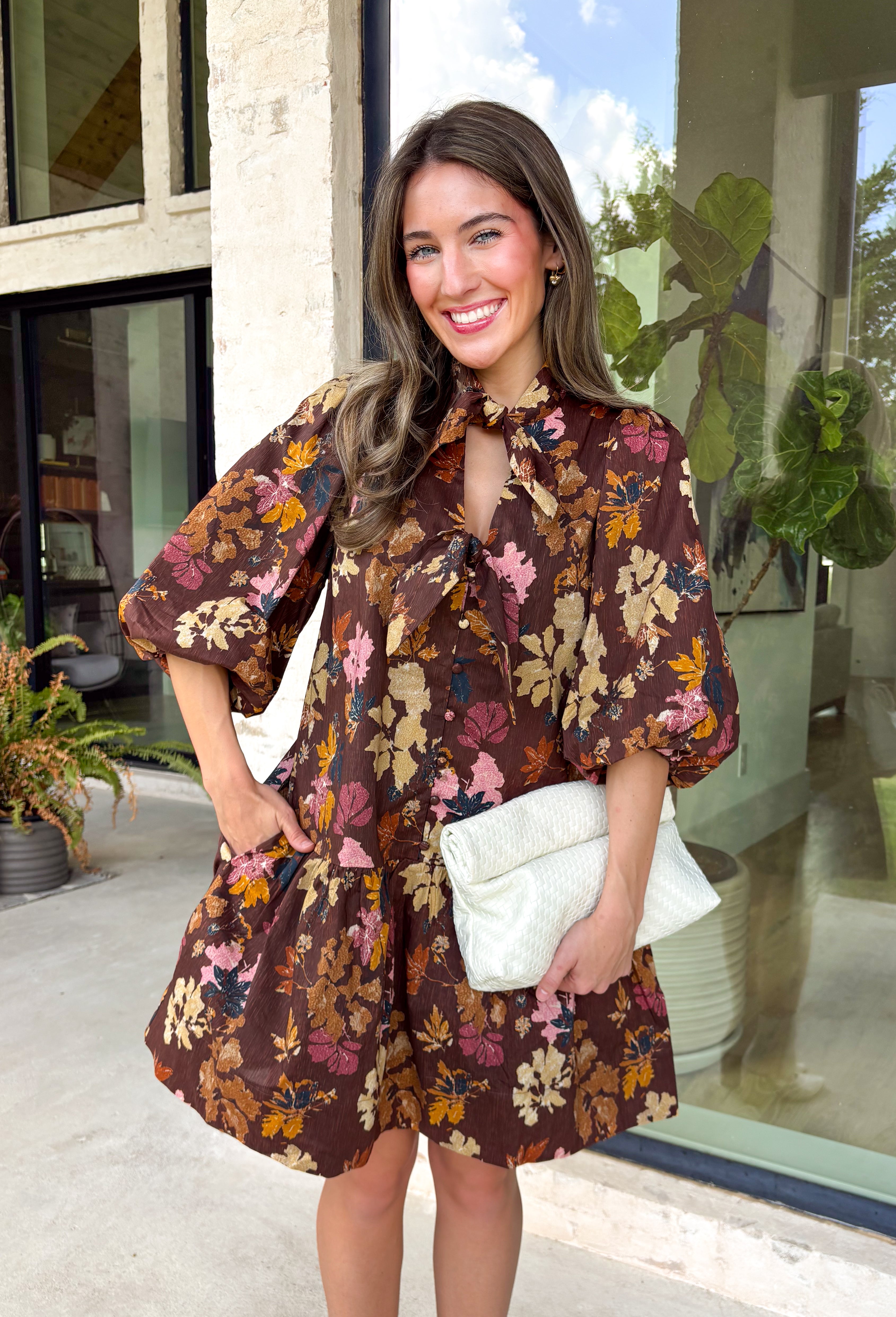 Capture the beauty of the season in this effortlessly feminine dress from Entro. Designed with a rich brown backdrop and a fall-inspired floral print with delicate leaf-like details, this charming dress is perfect for everything from brunch dates to seasonal celebrations. The flattering v-neckline features sweet tie details at the neck and bust, while decorative front buttons add timeless appeal. 