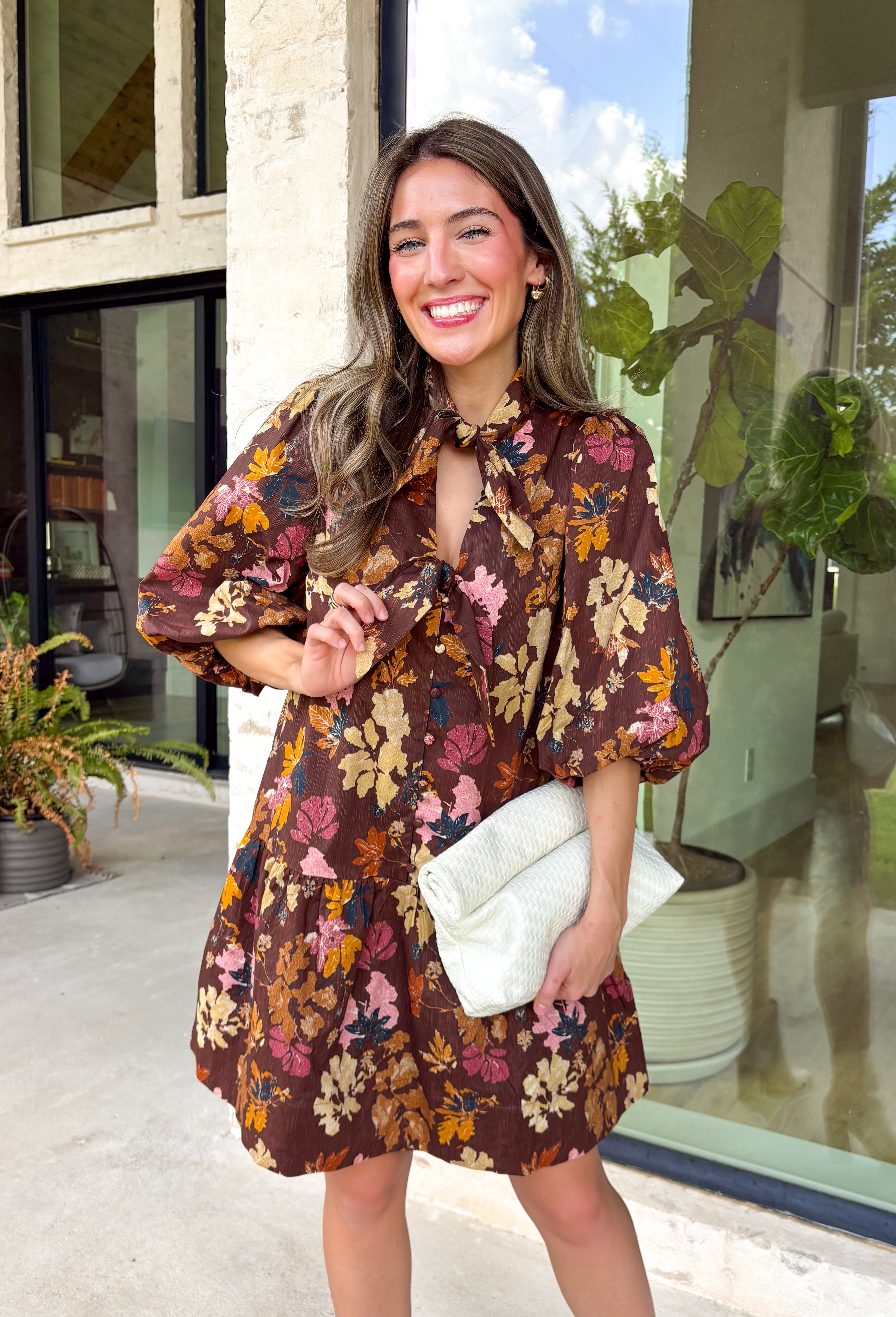 Capture the beauty of the season in this effortlessly feminine dress from Entro. Designed with a rich brown backdrop and a fall-inspired floral print with delicate leaf-like details, this charming dress is perfect for everything from brunch dates to seasonal celebrations. The flattering v-neckline features sweet tie details at the neck and bust, while decorative front buttons add timeless appeal. 