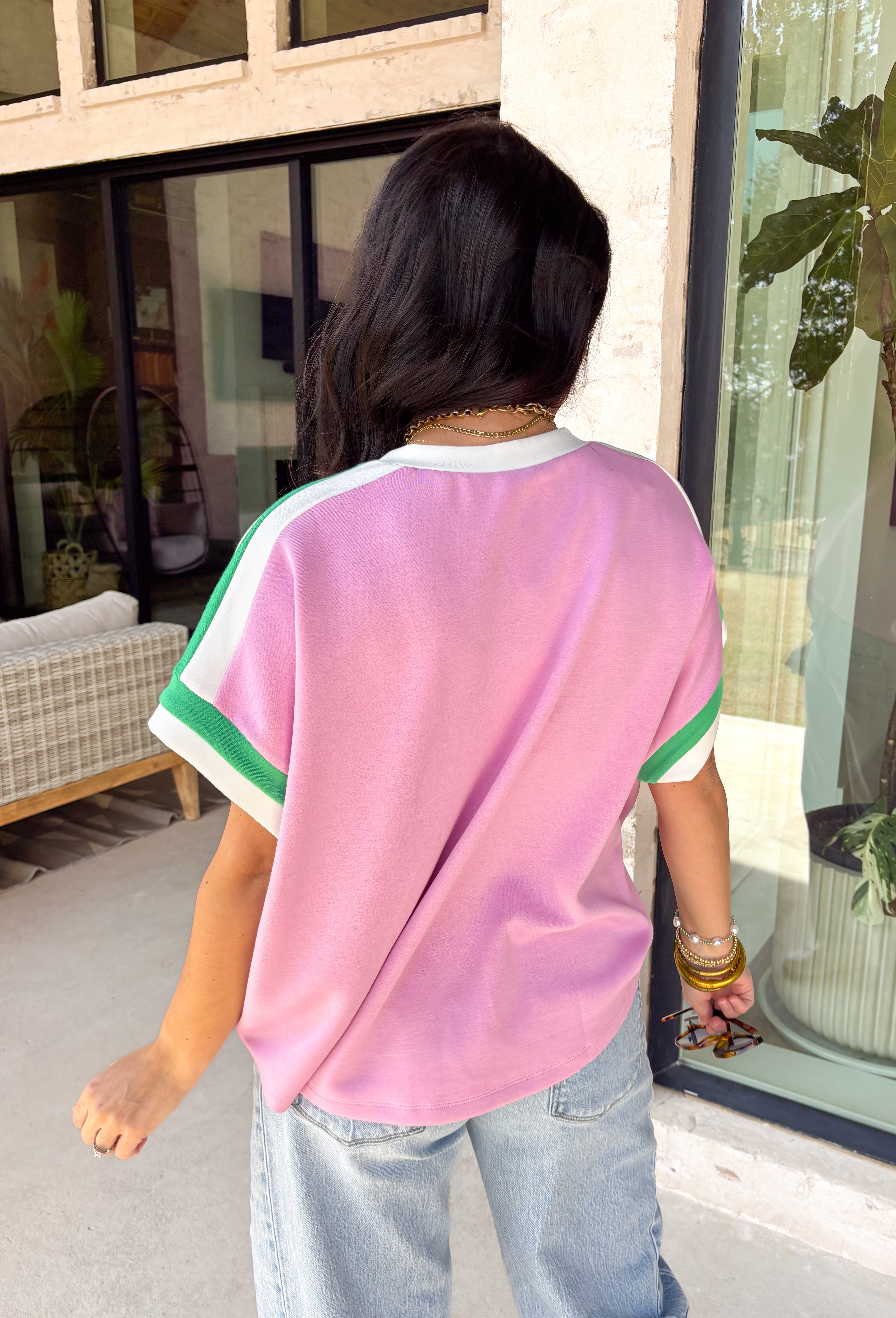 Cute, comfy, and just the right amount of sporty, this pink short sleeve knit top by Entro is such a fun spring staple. The green and white contrast trim along the neckline, sleeves, and shoulders gives it that fresh pop of color that makes even your simplest outfit feel styled. It’s lightweight with a soft, stretchy feel, making it perfect for busy days when you want to look put-together but stay comfortable. Pair it with denim shorts, white jeans, or even a casual skirt.