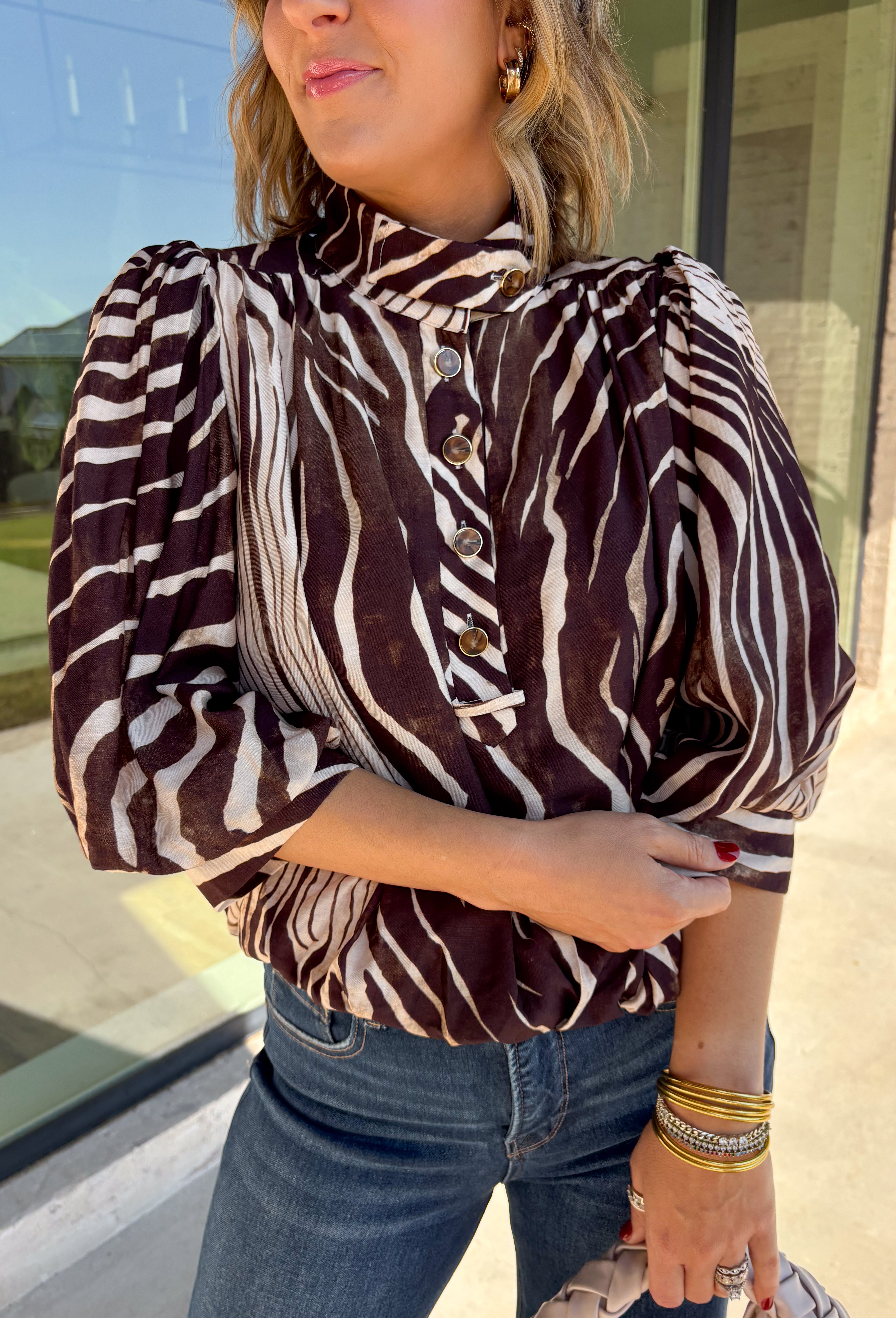 Neutral gets a little wild with this brown and cream zebra print blouse from Entro. The warm color combination makes the statement print easy to style while fitting perfectly into the transition from fall into winter. A stand collar and partial button-front closure give the lightweight silhouette a classic touch, while gathered detailing at the shoulders and back adds shape and movement.