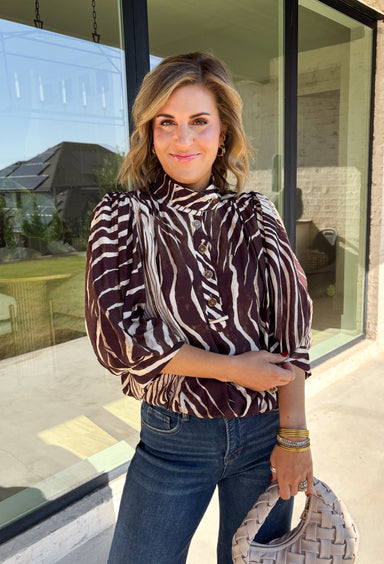 Neutral gets a little wild with this brown and cream zebra print blouse from Entro. The warm color combination makes the statement print easy to style while fitting perfectly into the transition from fall into winter. A stand collar and partial button-front closure give the lightweight silhouette a classic touch, while gathered detailing at the shoulders and back adds shape and movement.