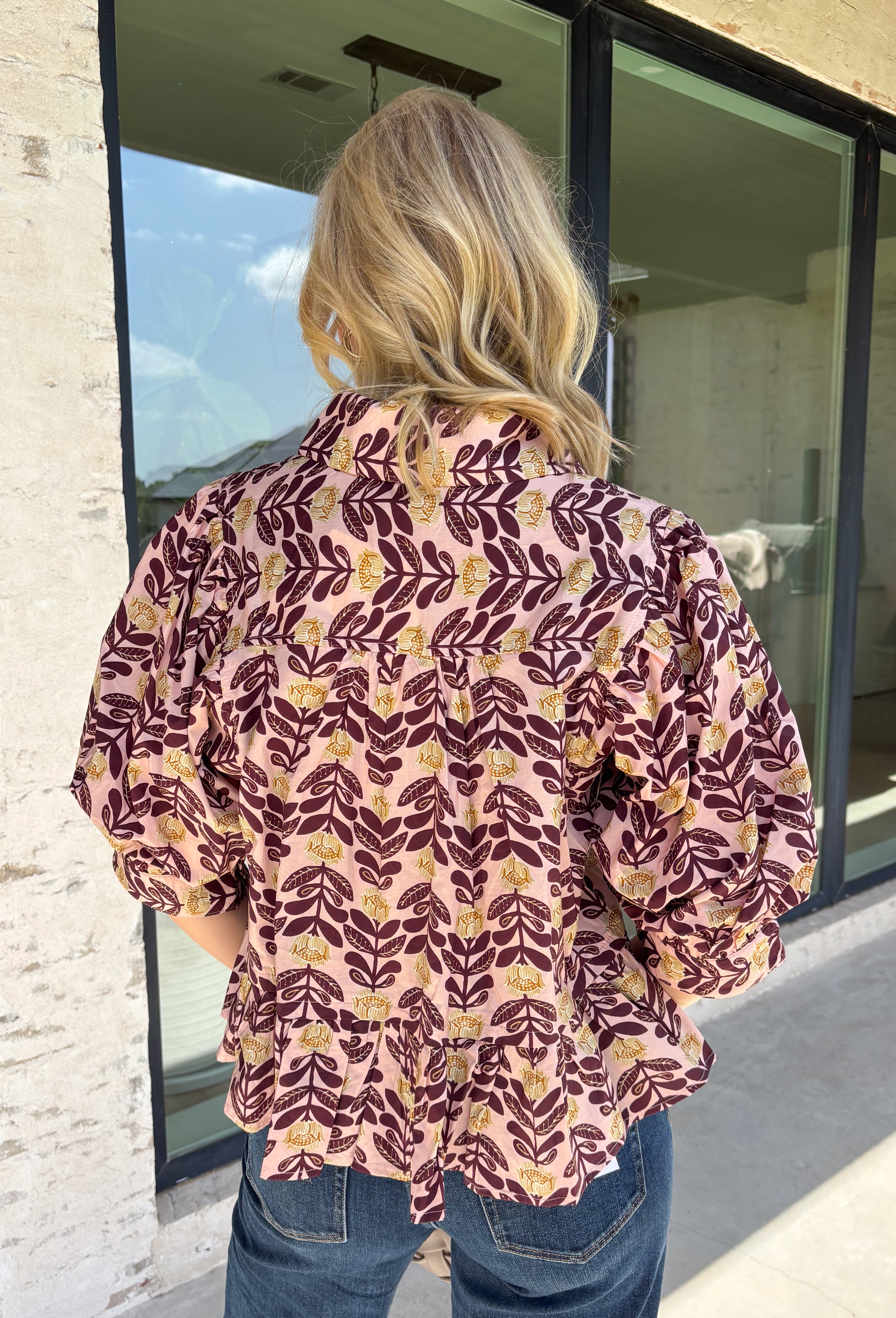 Soft, feminine, and full of seasonal charm, this floral blouse is an effortless addition to your fall wardrobe. Designed with a beautiful blush backdrop and a rich burgundy and tan floral print, this top brings together warm autumn hues in a timeless silhouette. The button-front design adds classic appeal, while the ruffle hem creates a flattering, feminine finish. Gathered detailing at the back yoke gives this blouse a relaxed, flowy fit that's perfect for everything from workdays to weekend outings.