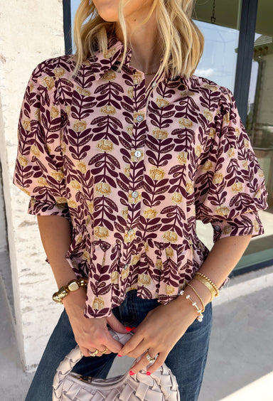 Soft, feminine, and full of seasonal charm, this floral blouse is an effortless addition to your fall wardrobe. Designed with a beautiful blush backdrop and a rich burgundy and tan floral print, this top brings together warm autumn hues in a timeless silhouette. The button-front design adds classic appeal, while the ruffle hem creates a flattering, feminine finish. Gathered detailing at the back yoke gives this blouse a relaxed, flowy fit that's perfect for everything from workdays to weekend outings.
