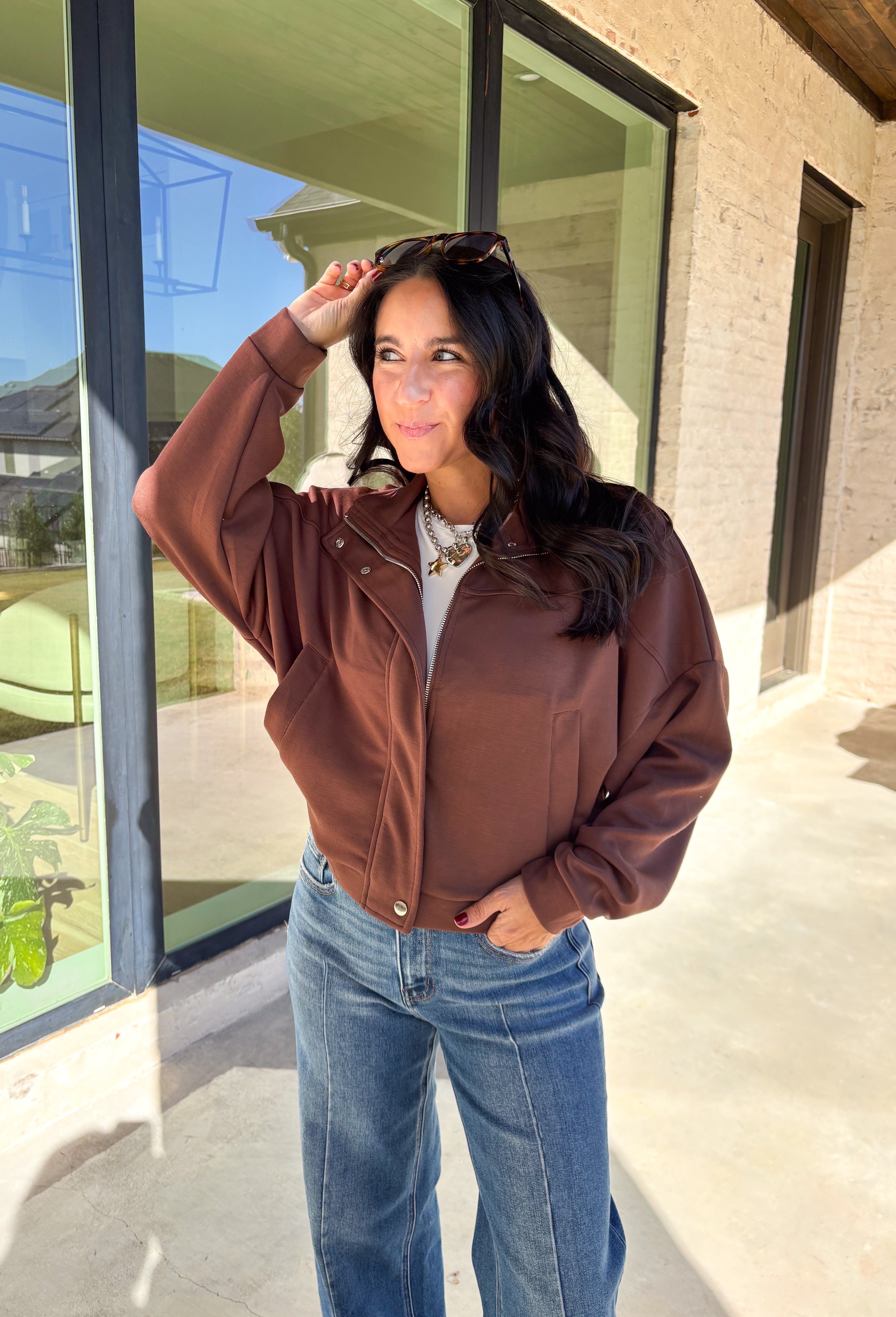 Add a touch of effortless cool to your winter wardrobe with this chocolate brown bomber jacket by Iris. Designed with a cropped silhouette and soft dolman sleeves, it’s a modern twist on a classic favorite. The snap collar, front pockets, and zip closure give it that timeless bomber edge, while the cozy fabric blend keeps it soft and easy to wear all season long.