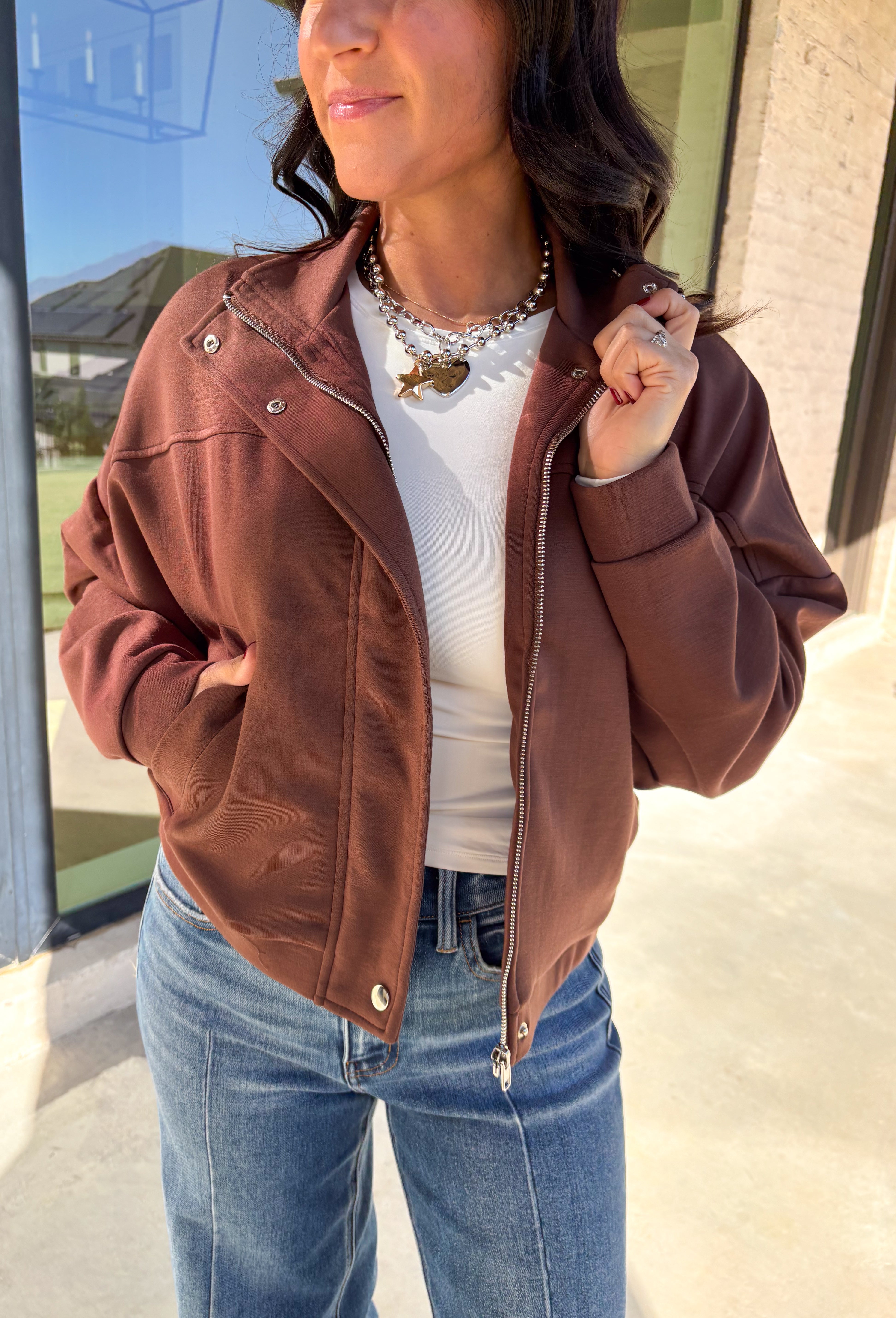 Add a touch of effortless cool to your winter wardrobe with this chocolate brown bomber jacket by Iris. Designed with a cropped silhouette and soft dolman sleeves, it’s a modern twist on a classic favorite. The snap collar, front pockets, and zip closure give it that timeless bomber edge, while the cozy fabric blend keeps it soft and easy to wear all season long.