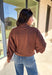 Add a touch of effortless cool to your winter wardrobe with this chocolate brown bomber jacket by Iris. Designed with a cropped silhouette and soft dolman sleeves, it’s a modern twist on a classic favorite. The snap collar, front pockets, and zip closure give it that timeless bomber edge, while the cozy fabric blend keeps it soft and easy to wear all season long.