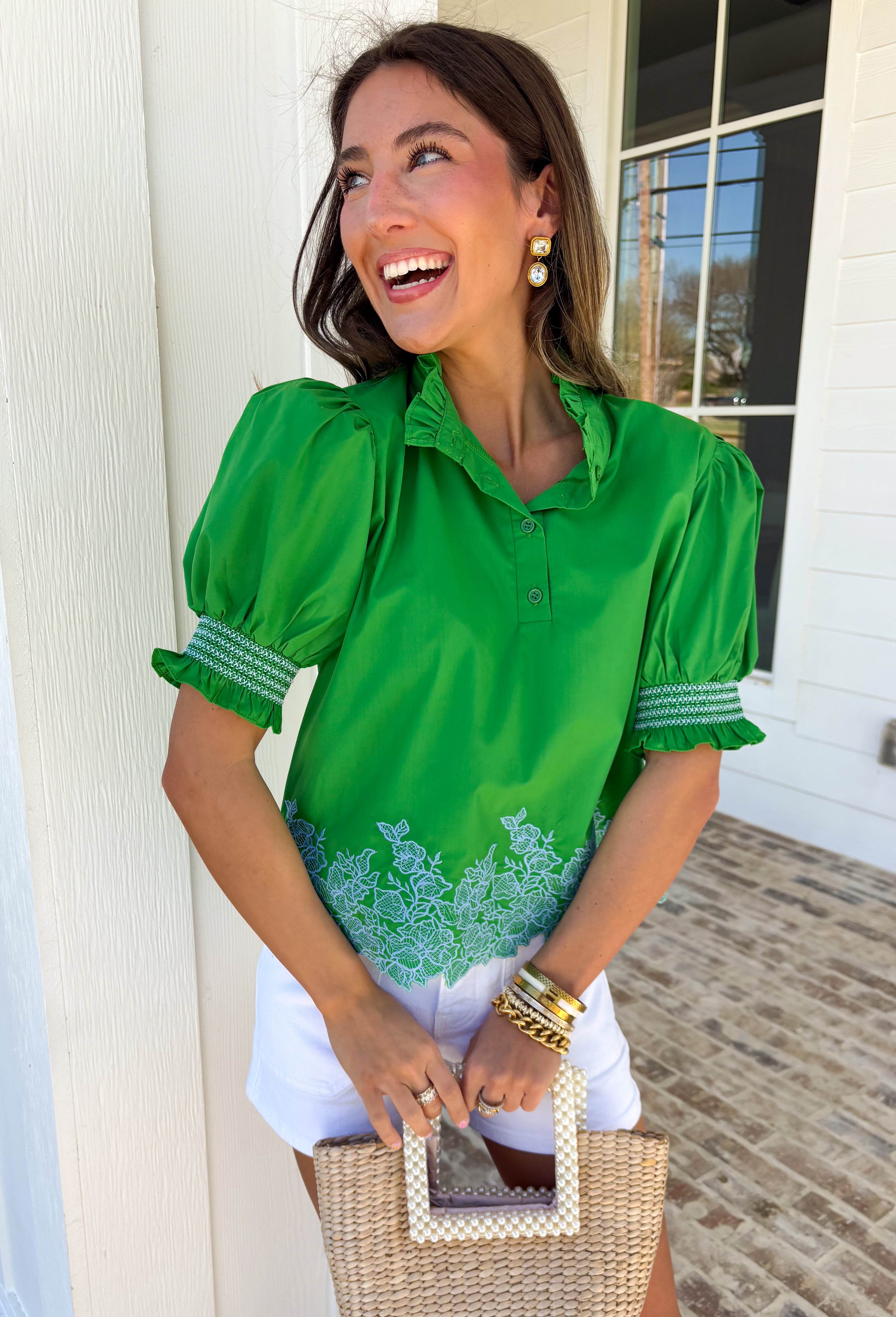 This green embroidered top is giving all the charming, autumnal details you love. The short sleeves feature smocked cuffs for a soft, feminine touch, while the blue embroidered border hem adds a pop of color that makes the whole look stand out. The ruffle band collar with button closure keeps it sweet and polished, perfect for pairing with jeans or layering under a cardigan as the weather cools. Lightweight and easy to wear, it’s a piece you’ll reach for again and again this season.