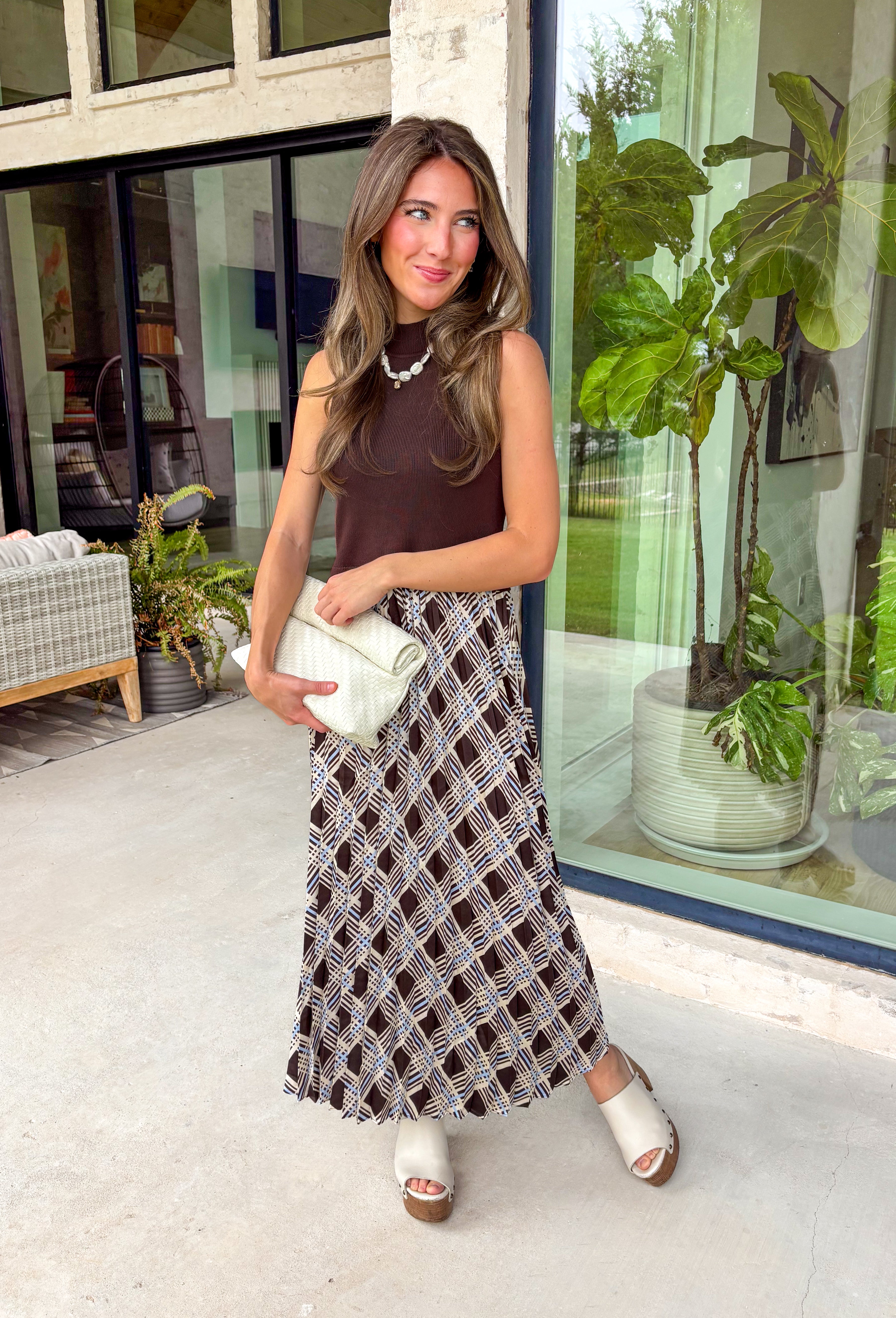 Elevate your fall wardrobe with this effortlessly elegant midi dress from Skies Are Blue. Featuring a rich brown sleeveless knit bodice with a classic mock neckline, this dress is beautifully complemented by a flowing pleated skirt showcasing an abstract print with subtle pops of blue. The combination of textures creates a polished, sophisticated look that's both comfortable and eye-catching. 