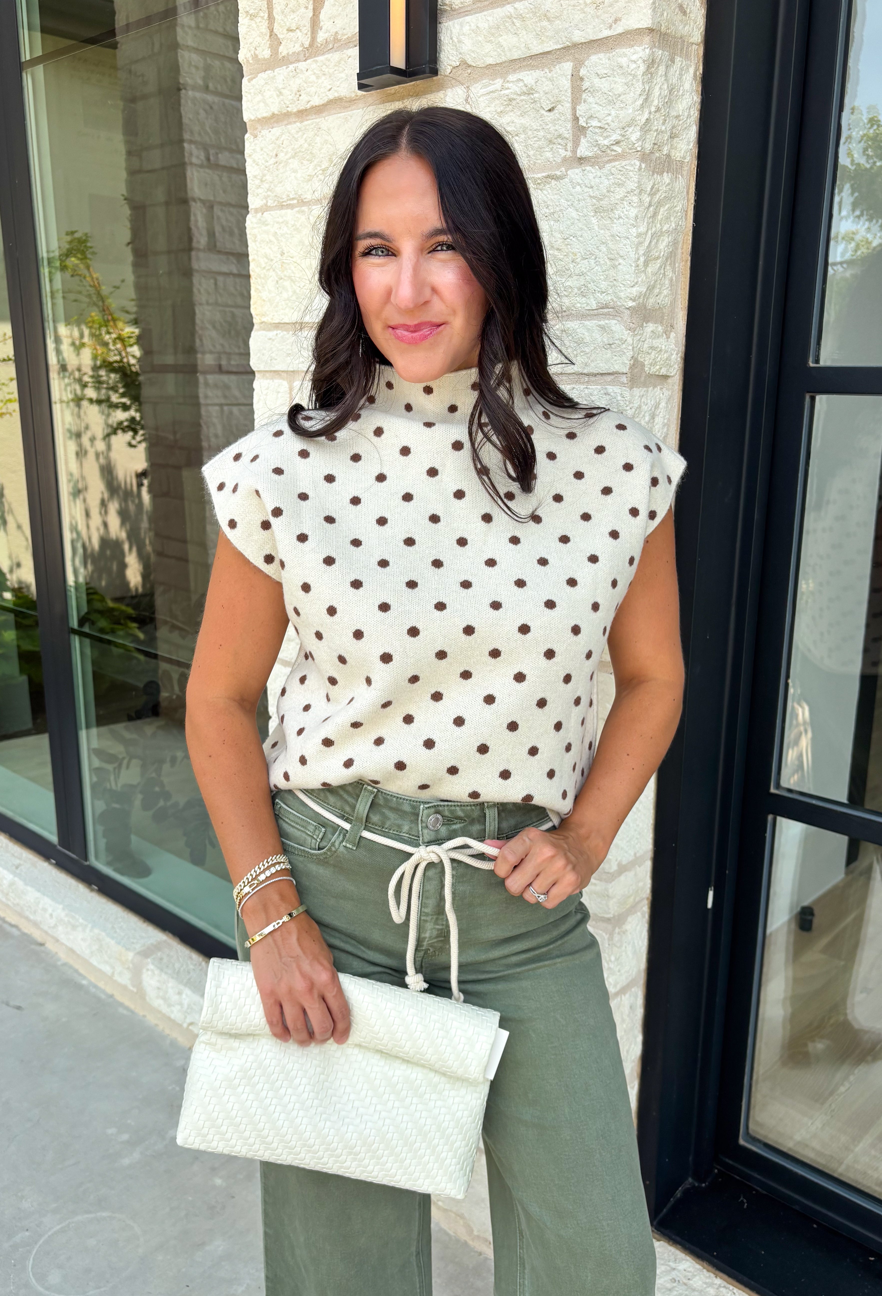 Classic polka dots get a cozy fall makeover in this adorable sleeveless sweater. Featuring a soft ecru knit with rich brown polka dots, this timeless top is equal parts playful and polished. The mock neckline and cap sleeve detail create an elevated silhouette, while the soft sweater knit makes it perfect for layering throughout the season. Wear it on its own during mild autumn days or layer it under your favorite jacket or blazer as the temperatures begin to cool.