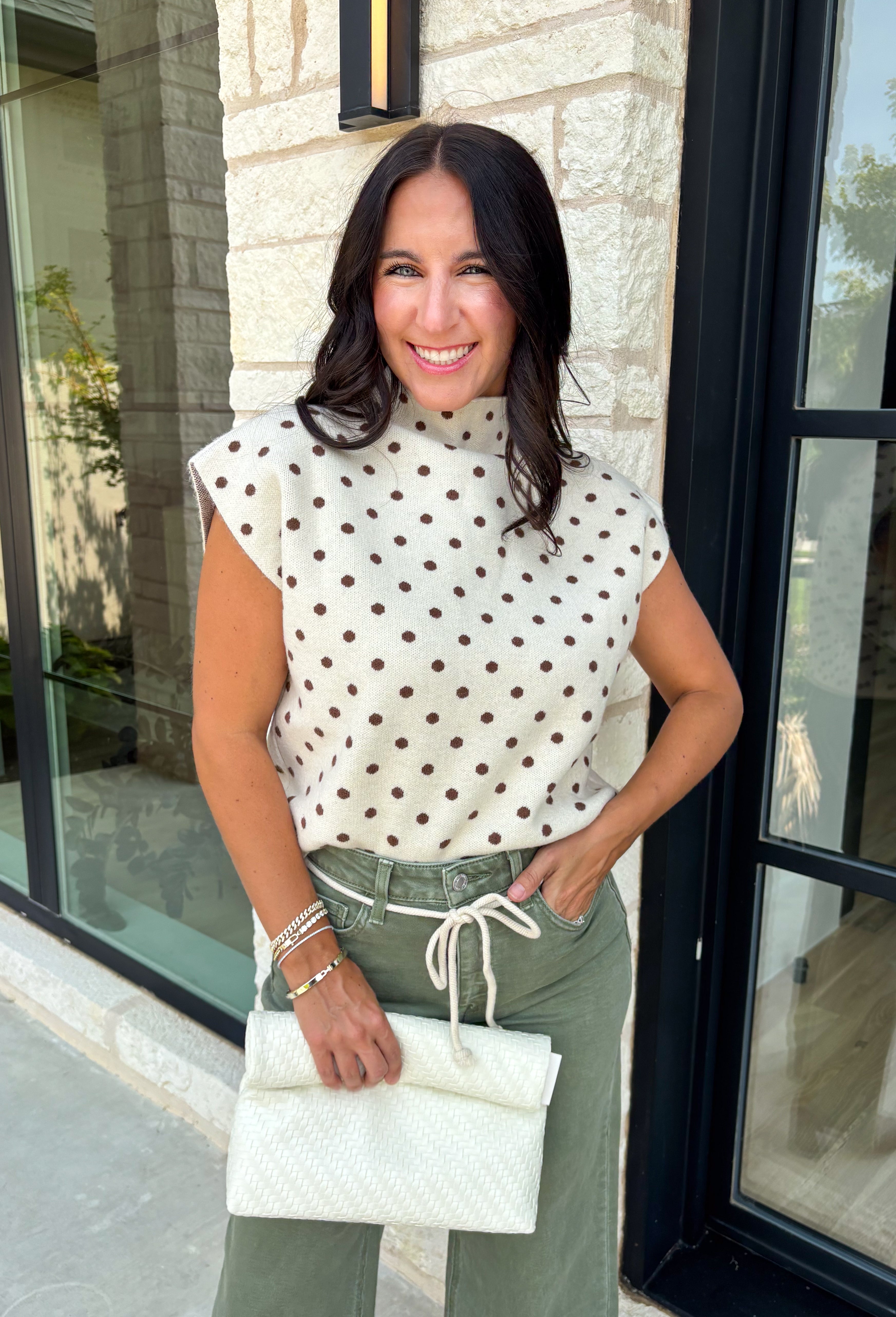 Classic polka dots get a cozy fall makeover in this adorable sleeveless sweater. Featuring a soft ecru knit with rich brown polka dots, this timeless top is equal parts playful and polished. The mock neckline and cap sleeve detail create an elevated silhouette, while the soft sweater knit makes it perfect for layering throughout the season. Wear it on its own during mild autumn days or layer it under your favorite jacket or blazer as the temperatures begin to cool.