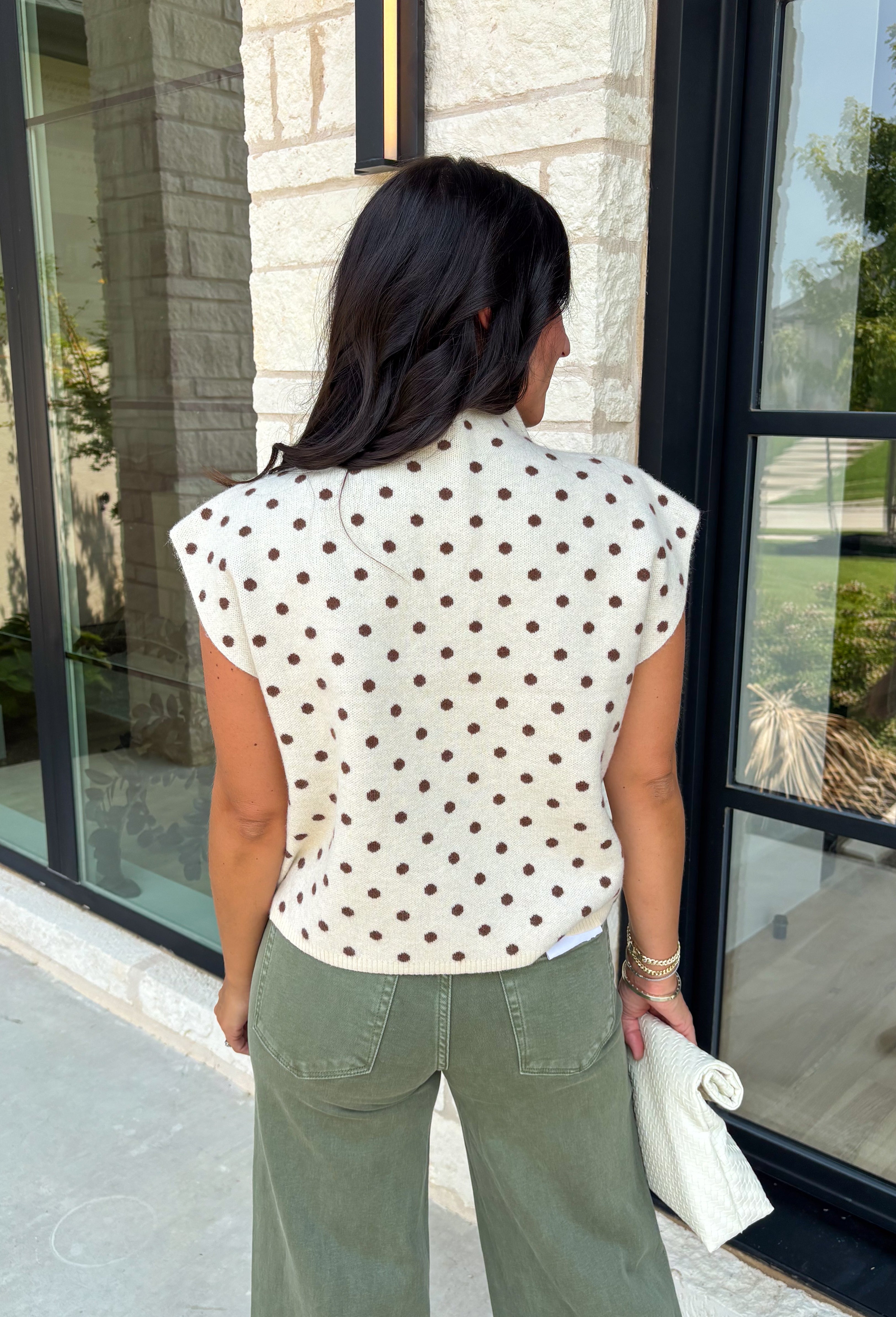 Classic polka dots get a cozy fall makeover in this adorable sleeveless sweater. Featuring a soft ecru knit with rich brown polka dots, this timeless top is equal parts playful and polished. The mock neckline and cap sleeve detail create an elevated silhouette, while the soft sweater knit makes it perfect for layering throughout the season. Wear it on its own during mild autumn days or layer it under your favorite jacket or blazer as the temperatures begin to cool.