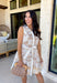 Soft, timeless, and perfect for spring days, this sleeveless tan dress is an effortless go-to for looking put together with minimal effort. Featuring a white floral print throughout, it has a fresh, neutral feel that’s easy to dress up or keep casual. The hidden button-down design and collared neckline give it a classic touch, while white trim along the front adds a clean contrast detail. 