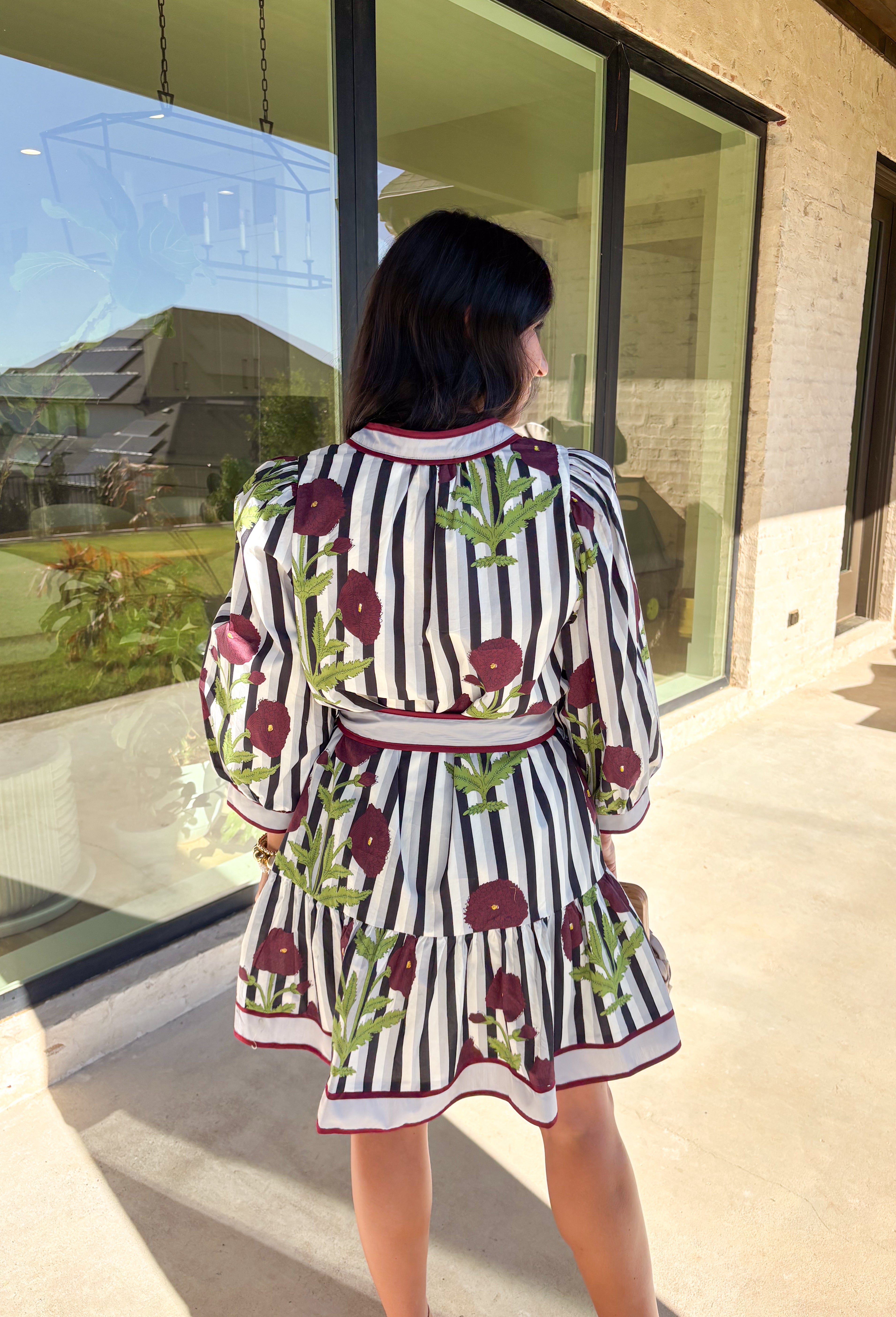 This floral stripe mini dress by Entro blends playful charm with seasonal flair. Featuring a gray, navy, light blue, off white and&nbsp; stripe base adorned with burgundy florals and green leaves, it’s the perfect balance of classic and bold. The ¾ puff sleeves add volume, while the v-neckline with contrast trim and adjustable self-tie belt create a flattering silhouette. A ruffle hem and side pockets finish the look, with a full cotton lining that makes it as practical as it is pretty.
