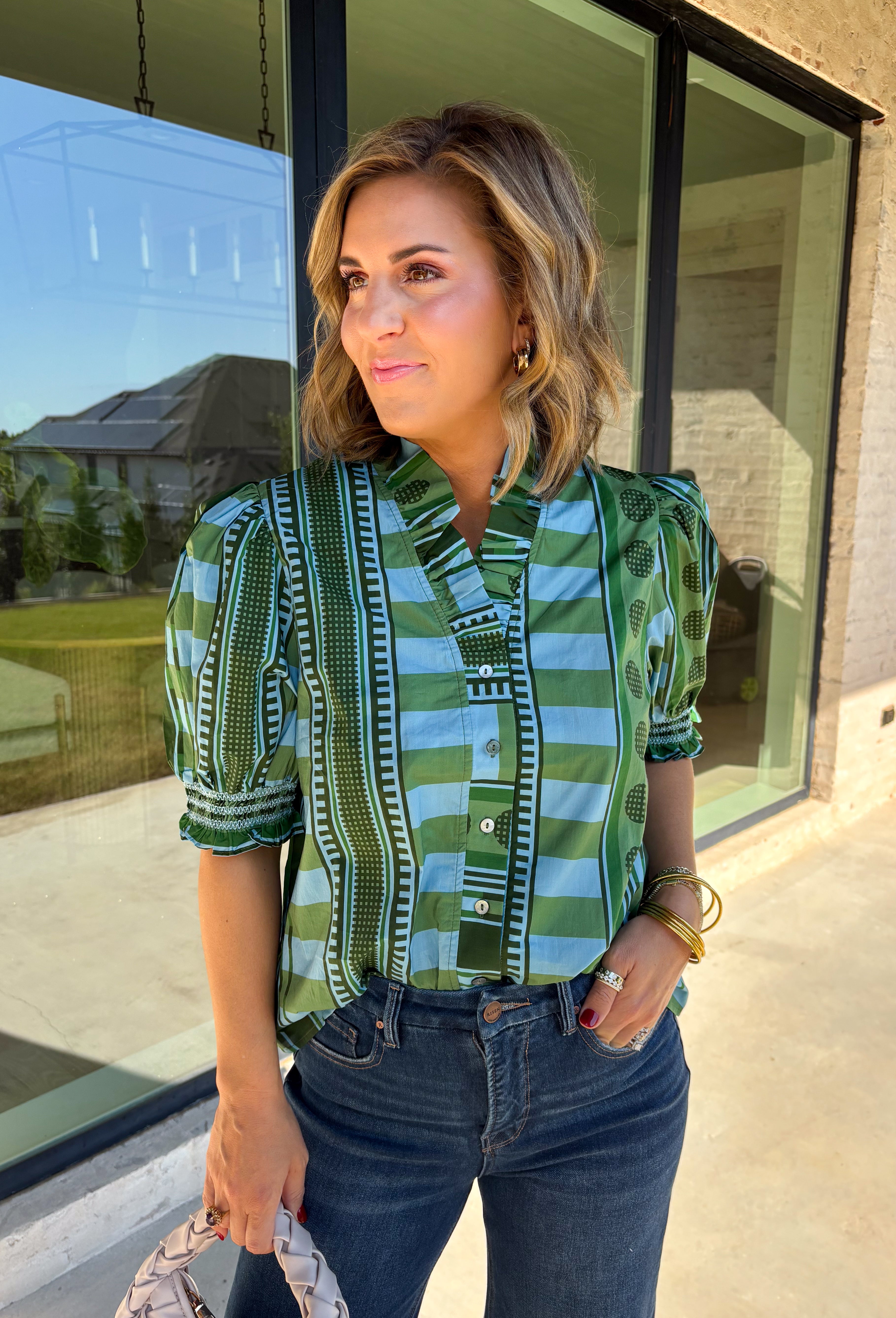 Bring playful pattern and timeless charm to your fall wardrobe with this beautifully detailed top from Entro. Featuring a unique mix of stripe and polka dot prints in rich shades of olive and blue, this eye-catching blouse is perfect for adding personality to your everyday style. The feminine ruffle neckline and button-front design create a polished look, while the short puff sleeves are finished with smocked ruffle cuffs for an extra touch of charm. 