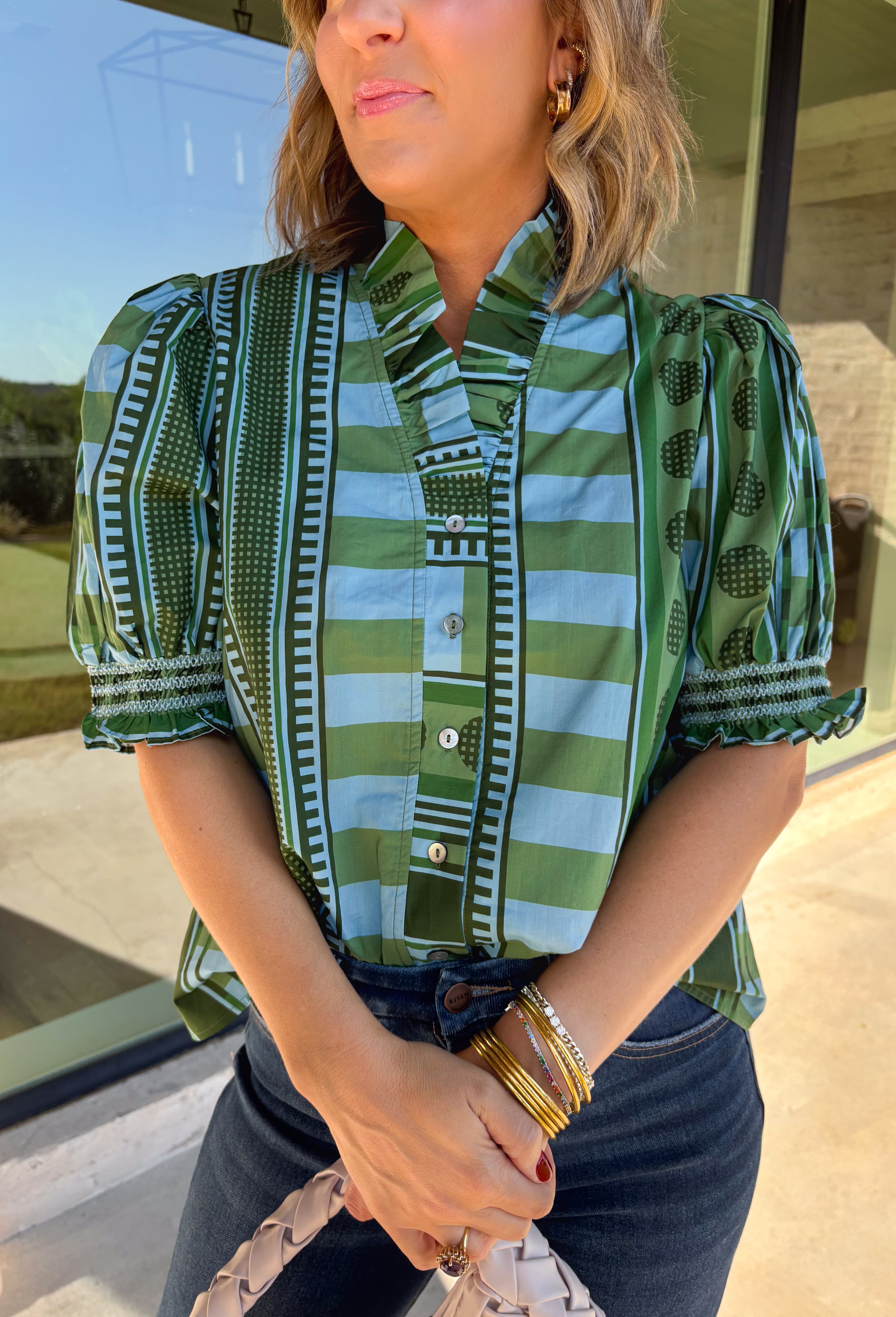 Bring playful pattern and timeless charm to your fall wardrobe with this beautifully detailed top from Entro. Featuring a unique mix of stripe and polka dot prints in rich shades of olive and blue, this eye-catching blouse is perfect for adding personality to your everyday style. The feminine ruffle neckline and button-front design create a polished look, while the short puff sleeves are finished with smocked ruffle cuffs for an extra touch of charm. 