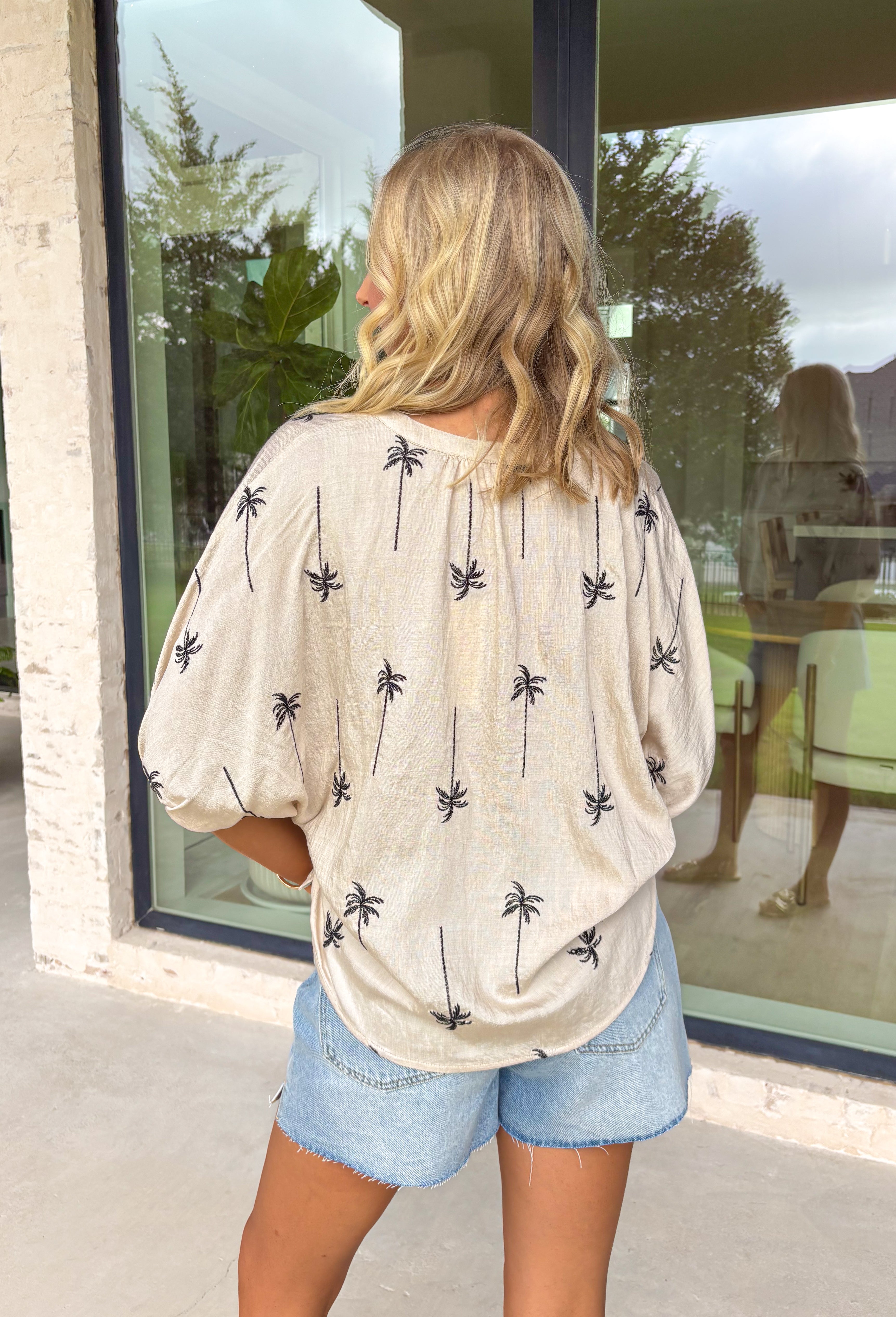 Easy, elevated, and just a little bit tropical! This neutral short sleeve button down top features delicate black embroidered palm trees for a subtle statement that still feels timeless. The contrast embroidery pops beautifully against the soft neutral base, giving it that relaxed coastal vibe without being over the top. Lightweight and drapey, this top feels polished enough for dinner plans but effortless enough for everyday wear. 
