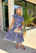 Fresh, charming, and full of thoughtful details, this blue button-down midi dress by Entro feels like spring in dress form. Featuring an off-white floral print with delicate mini star accents throughout, it strikes the perfect balance between playful and classic. The blue and white striped collar and trim add a crisp contrast, while the matching self-tie waist creates a flattering, easy fit. 