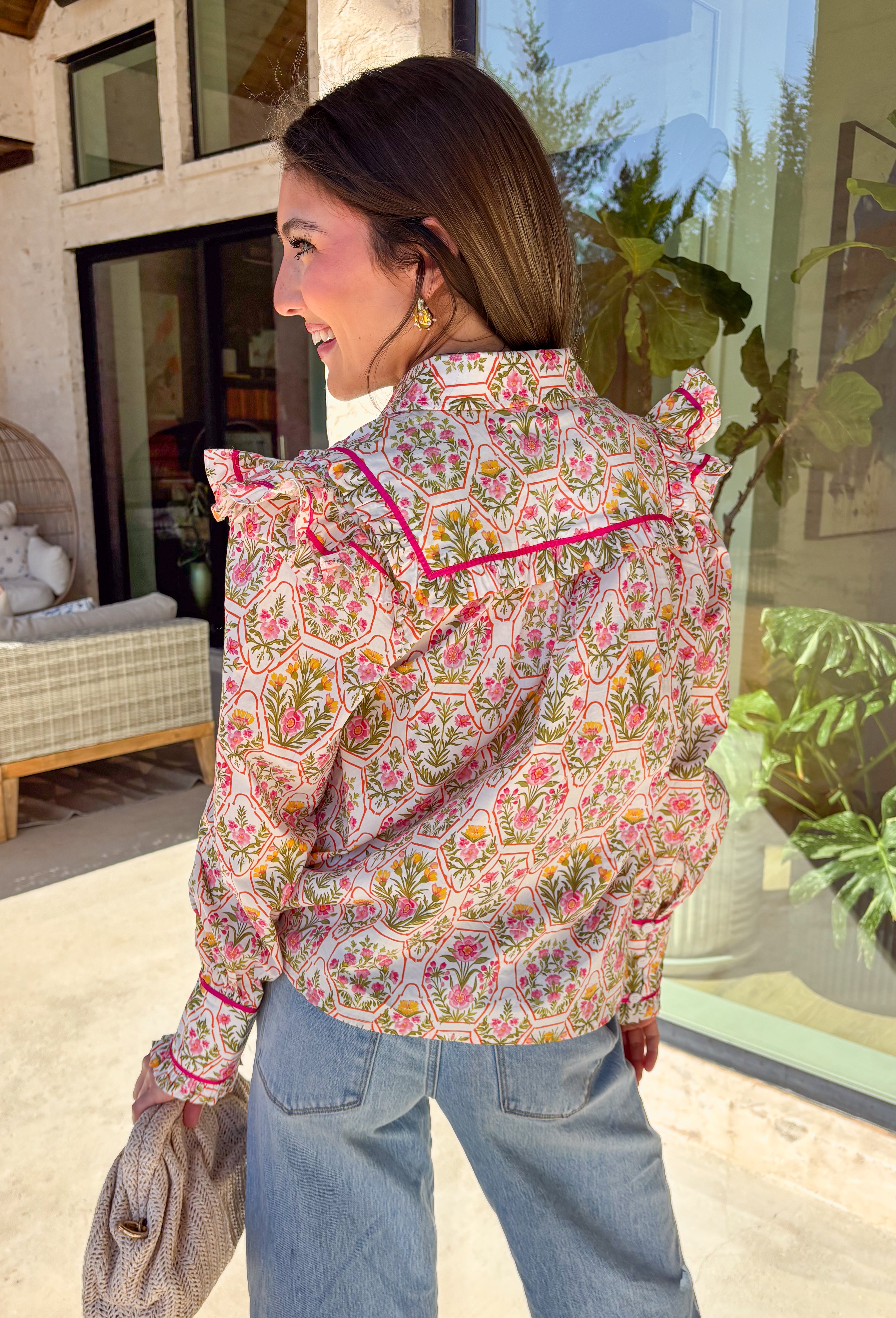 This off-white button down top is bursting with fresh spring energy thanks to its vibrant floral print and playful details. Splashes of green, pink, orange, and yellow bring a cheerful pop of color, while the ruffle sleeves add a soft, feminine touch that feels effortlessly polished. Designed with a classic collared neckline and lightweight cotton fabric, this top is perfect for bright days, brunch plans, and easy everyday styling. 