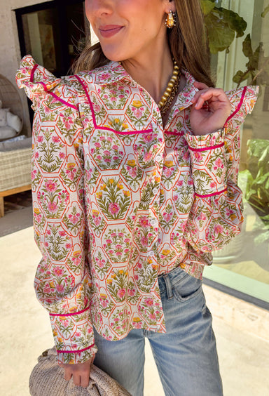 This off-white button down top is bursting with fresh spring energy thanks to its vibrant floral print and playful details. Splashes of green, pink, orange, and yellow bring a cheerful pop of color, while the ruffle sleeves add a soft, feminine touch that feels effortlessly polished. Designed with a classic collared neckline and lightweight cotton fabric, this top is perfect for bright days, brunch plans, and easy everyday styling. 