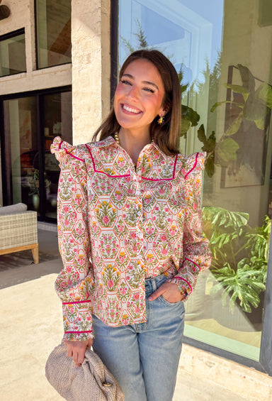 This off-white button down top is bursting with fresh spring energy thanks to its vibrant floral print and playful details. Splashes of green, pink, orange, and yellow bring a cheerful pop of color, while the ruffle sleeves add a soft, feminine touch that feels effortlessly polished. Designed with a classic collared neckline and lightweight cotton fabric, this top is perfect for bright days, brunch plans, and easy everyday styling. 