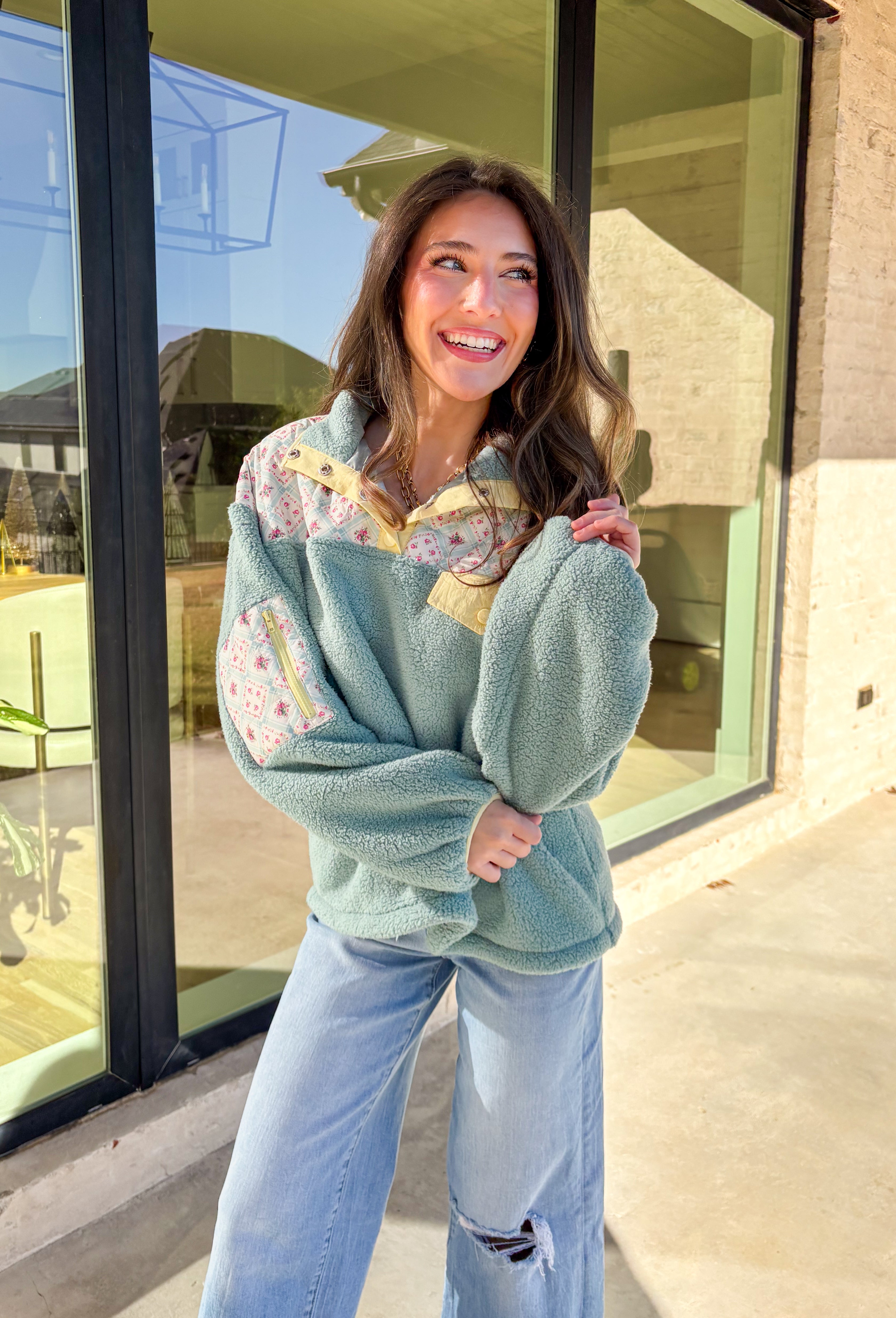 Cozy meets fresh in this sage sherpa pullover by New In — the perfect layer for cool spring mornings and breezy evenings. Designed with a soft sherpa body, this pullover features a floral quilted print along the top for a sweet seasonal touch. Pale yellow trim at the quarter button closure and a matching front pocket add a cheerful pop of color, making this piece feel bright, playful, and easy to wear as the seasons change.