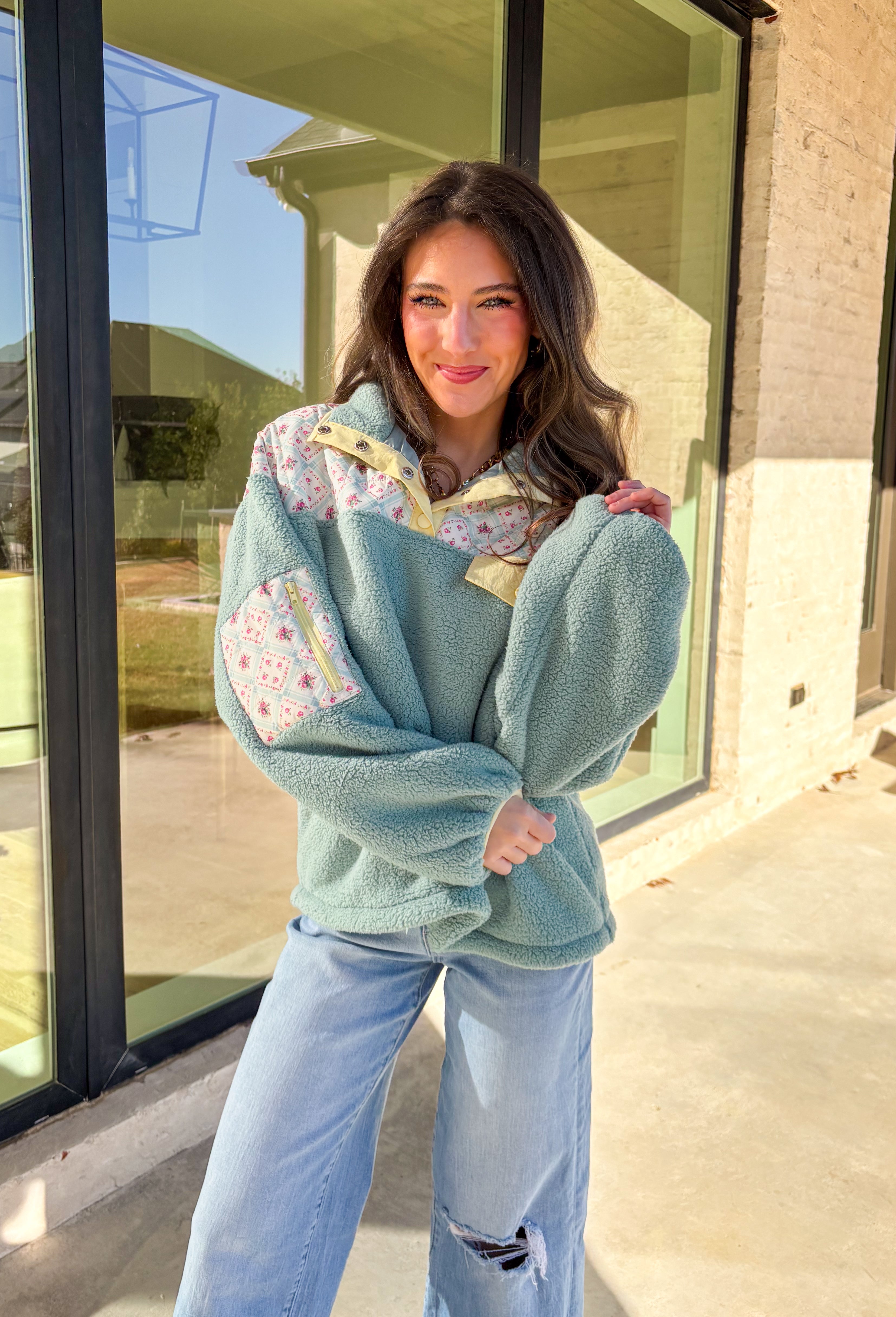 Cozy meets fresh in this sage sherpa pullover by New In — the perfect layer for cool spring mornings and breezy evenings. Designed with a soft sherpa body, this pullover features a floral quilted print along the top for a sweet seasonal touch. Pale yellow trim at the quarter button closure and a matching front pocket add a cheerful pop of color, making this piece feel bright, playful, and easy to wear as the seasons change.