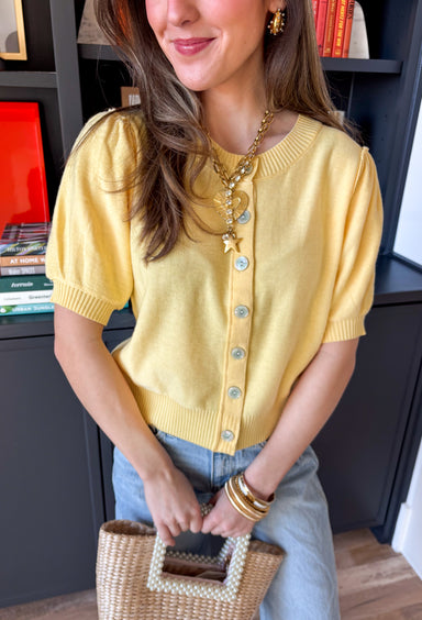 Soft, sunny, and perfect for spring layering, this butter yellow button-down knit top by Entro brings a warm pop of color to your everyday wardrobe. The lightweight knit feels cozy without being heavy, making it ideal for those in-between spring days. Ribbed detailing along the neckline, cuffs, and hem adds subtle texture and a polished finish, while the button-down design makes it easy to wear on its own or layered over a tank.