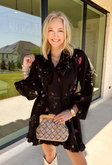 Feminine, chic, and full of seasonal charm, this floral dress is the perfect piece for all your favorite fall occasions. Featuring a classic black backdrop with a vibrant colorful floral print, this dress offers a timeless silhouette with eye-catching details. The flattering v-neckline is accented by a beautiful scarf tie that adds a polished, sophisticated touch, while the self-tie waist creates a customizable fit you'll love. 