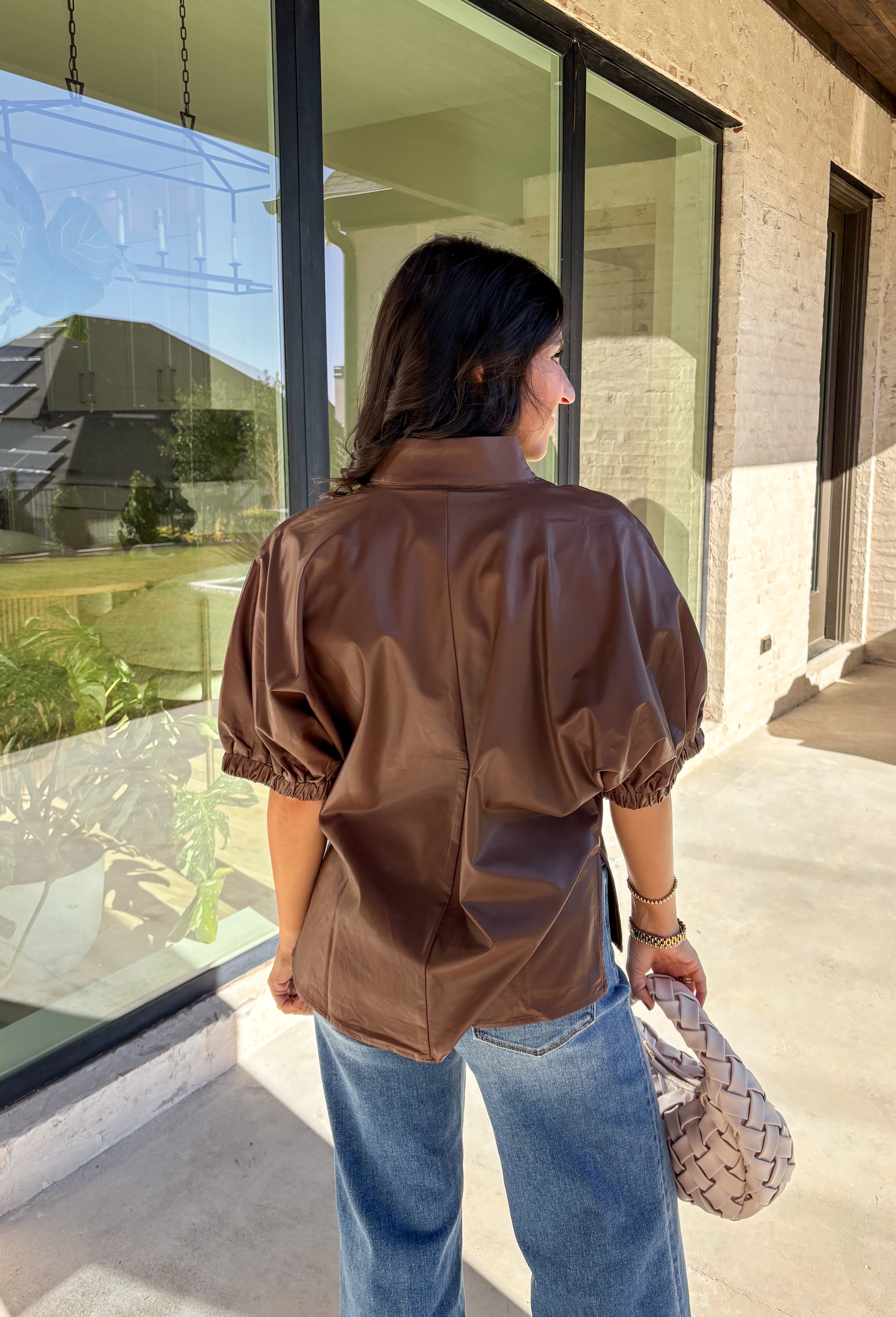 Elevate your wardrobe with this chic brown faux leather top by Entro. Designed with short puff sleeves and elasticated openings, it strikes the perfect balance of structured and feminine. The split v-neckline with a stand collar adds a modern edge, while the soft faux leather finish brings a touch of texture that feels fresh for the season. Perfect for dressing up denim or pairing with skirts, this top is a statement piece you’ll reach for again and again.