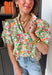Bright, fresh, and full of spring charm, this white short sleeve top by Entro is the perfect way to add a little color to your everyday look. The colorful floral print features happy pops of orange, green, and pink, while the subtle ruffle neckline keeps it sweet and feminine. Finished with pleated sleeve details and elastic cuffs, it has that “cute but still comfy” vibe we all love.