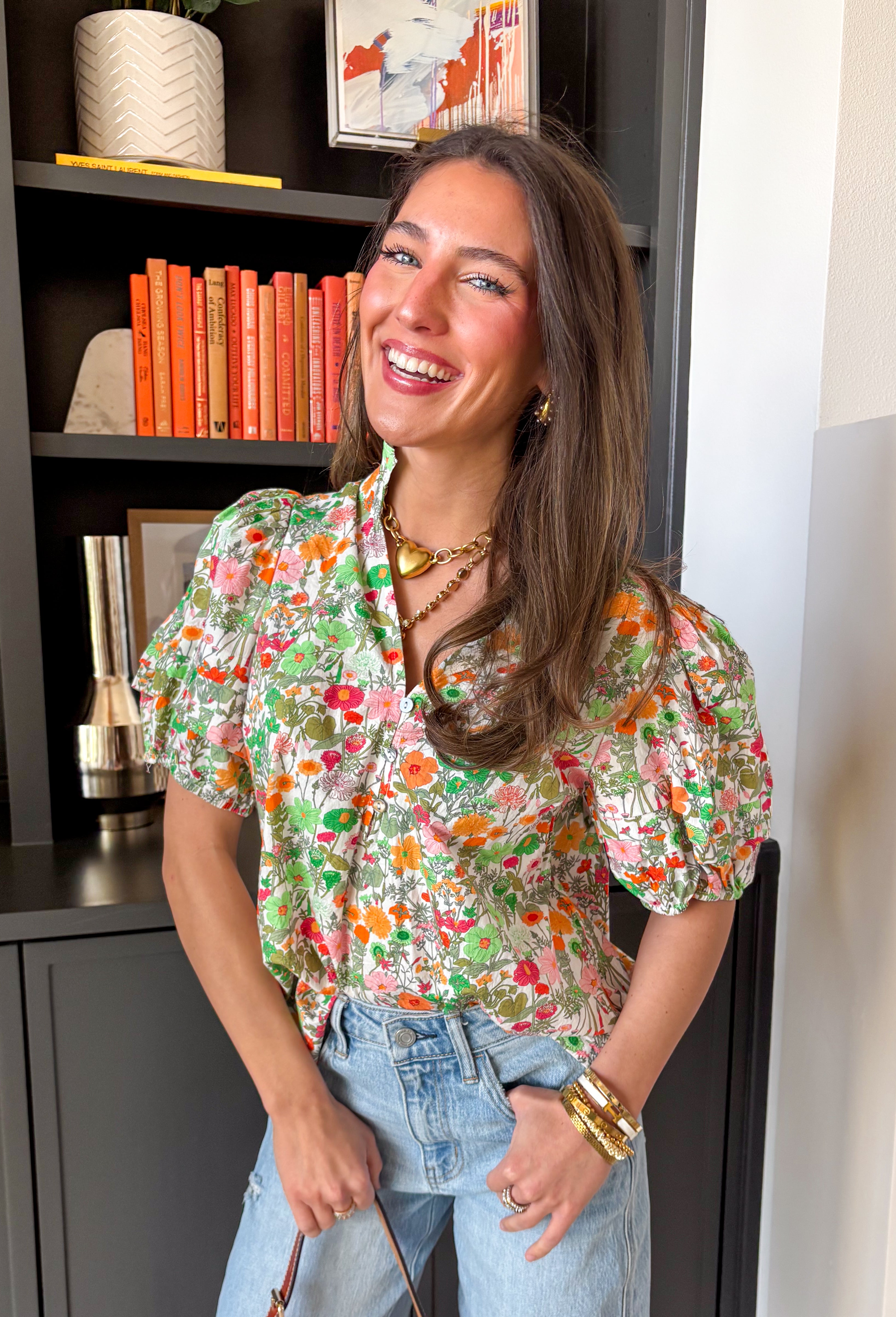Bright, fresh, and full of spring charm, this white short sleeve top by Entro is the perfect way to add a little color to your everyday look. The colorful floral print features happy pops of orange, green, and pink, while the subtle ruffle neckline keeps it sweet and feminine. Finished with pleated sleeve details and elastic cuffs, it has that “cute but still comfy” vibe we all love.