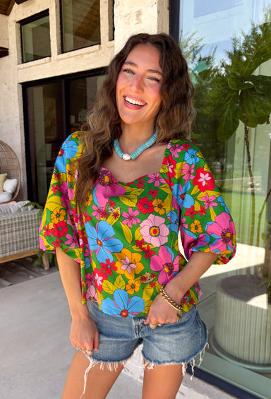 This green floral top is bursting with color and made for sunny summer days! Featuring a vibrant floral print in shades of pink, red, yellow, and blue, it instantly brightens up any outfit. The square neckline gives it a flattering, feminine feel, while the puff sleeves add just the right amount of charm. Finished with a sweet tie detail in the back, this lightweight cotton top is perfect for everything from brunch dates to weekend getaways. 