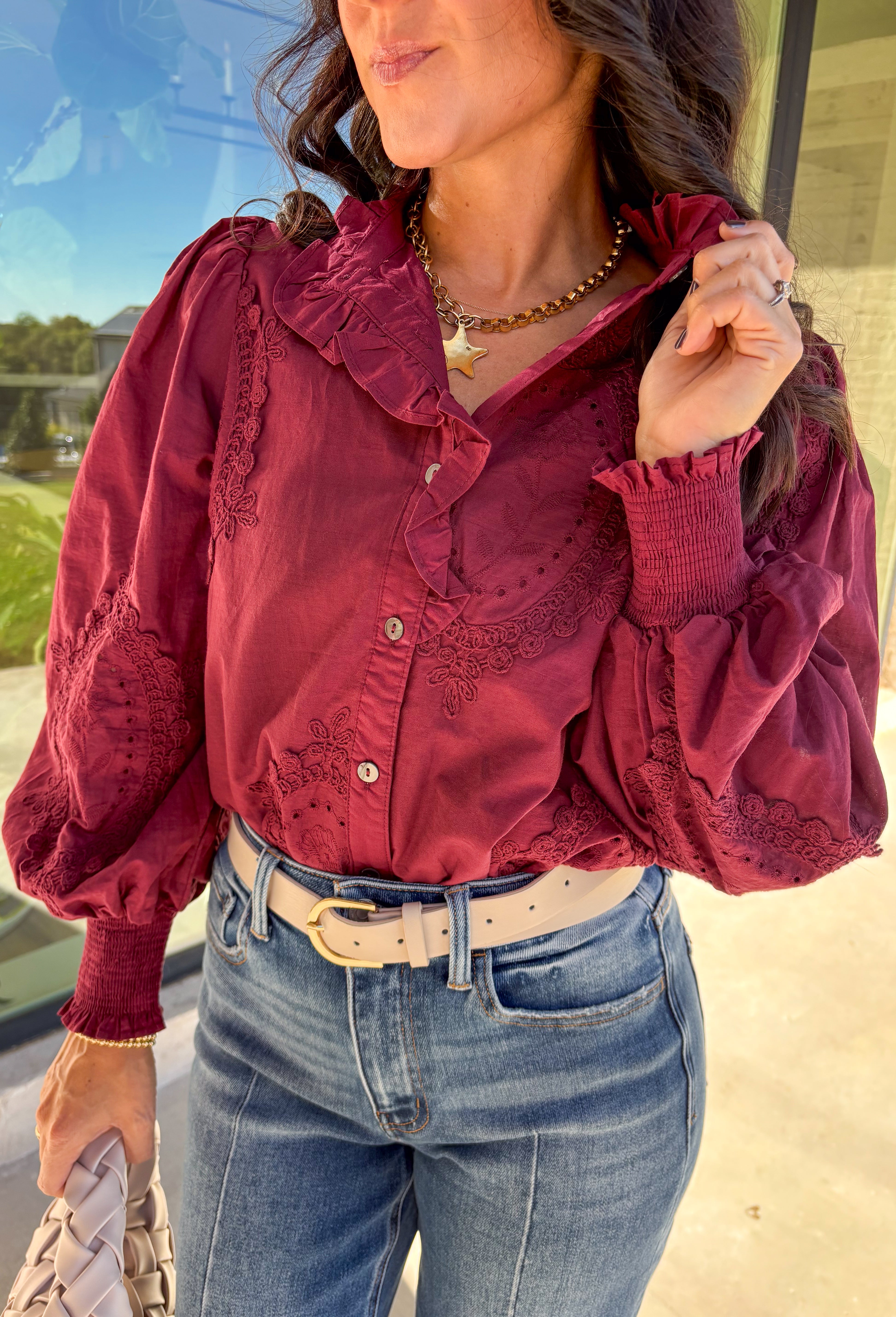 Timeless and full of detail, this burgundy top by Entro adds a refined touch to your fall wardrobe. Featuring an oval embroidered appliqué with eyelet accents, it’s beautifully designed to bring texture and depth to your look. The ruffled stand collar and smocked sleeve cuffs create a feminine finish, while the button-front closure keeps it classic and easy to style. Made from soft cotton, this top blends comfort and elegance effortlessly.
