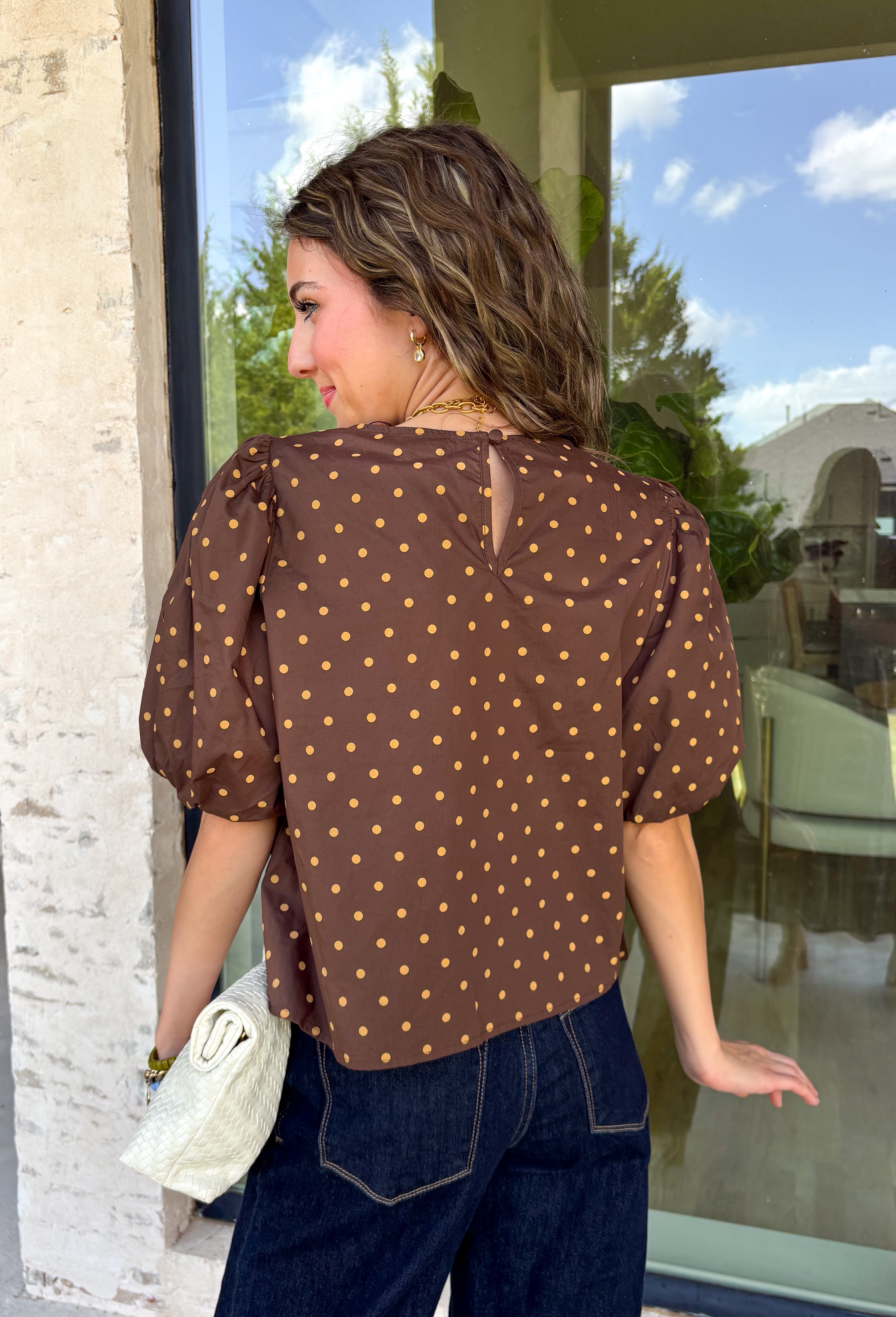 Classic polka dots never go out of style, and this charming top from Day + Moon is the perfect addition to your fall wardrobe. Designed in a rich brown hue with a timeless tan polka dot print, this effortlessly feminine blouse is easy to dress up or down. The puff sleeves add a soft, romantic touch, while the keyhole button closure at the back creates a polished finishing detail. Crafted from breathable cotton, this versatile top is perfect for everything from workdays to weekend outings.