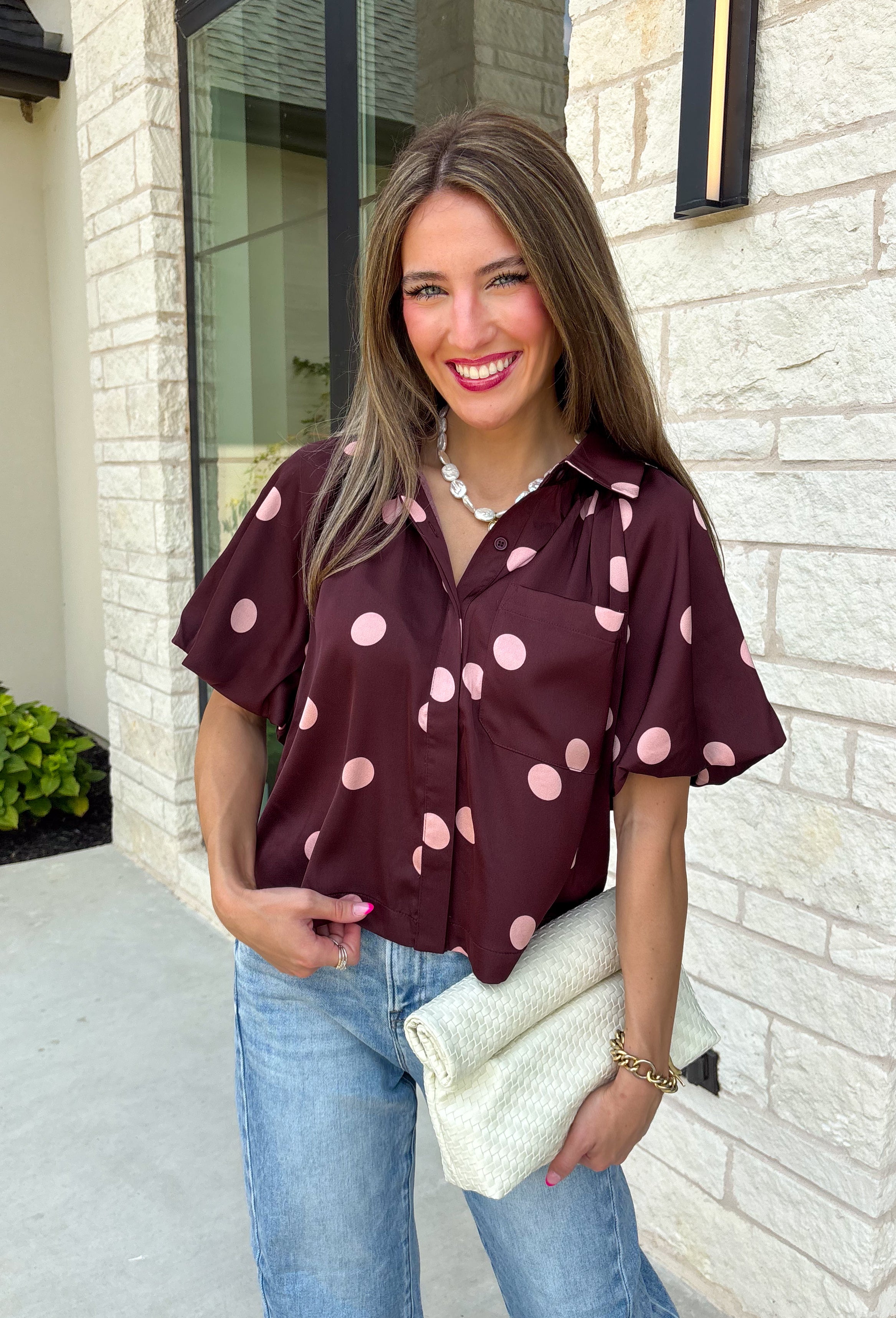 Classic polka dots meet rich fall color in this charming burgundy top! Featuring a soft mauve polka dot print, this top is an effortless way to add personality to your everyday wardrobe. The hidden button front creates a clean, polished look, while the foldover neckline and front pocket add timeless details you'll love. Finished with short puff sleeves, this versatile top is perfect for everything from workdays to weekend brunches and pairs beautifully with your favorite fall denim.