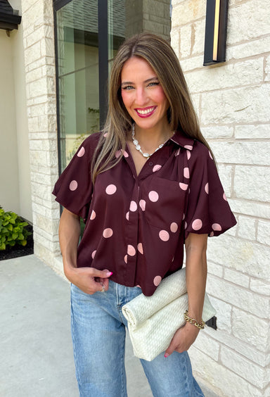 Classic polka dots meet rich fall color in this charming burgundy top! Featuring a soft mauve polka dot print, this top is an effortless way to add personality to your everyday wardrobe. The hidden button front creates a clean, polished look, while the foldover neckline and front pocket add timeless details you'll love. Finished with short puff sleeves, this versatile top is perfect for everything from workdays to weekend brunches and pairs beautifully with your favorite fall denim.