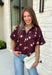 Classic polka dots meet rich fall color in this charming burgundy top! Featuring a soft mauve polka dot print, this top is an effortless way to add personality to your everyday wardrobe. The hidden button front creates a clean, polished look, while the foldover neckline and front pocket add timeless details you'll love. Finished with short puff sleeves, this versatile top is perfect for everything from workdays to weekend brunches and pairs beautifully with your favorite fall denim.