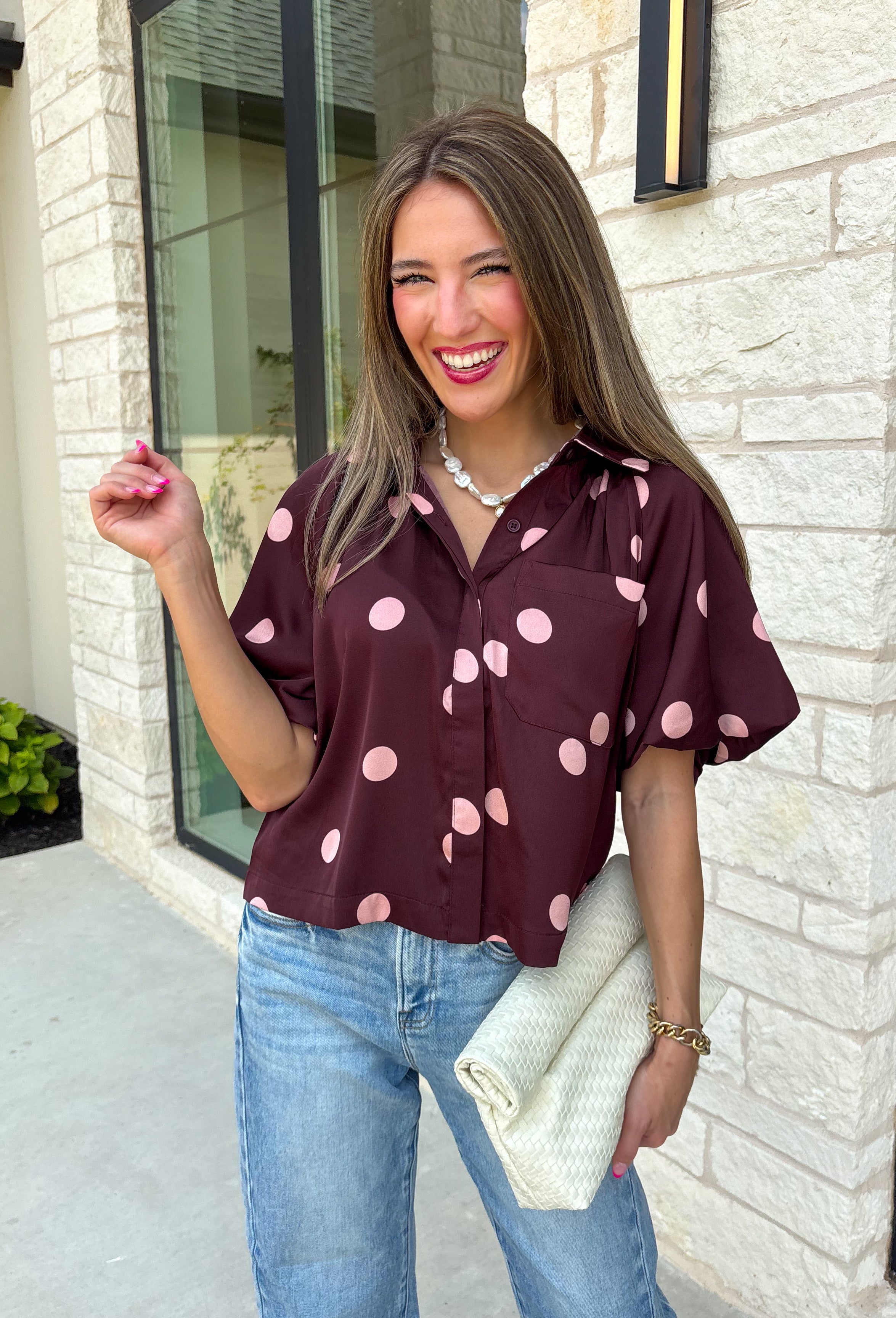 Classic polka dots meet rich fall color in this charming burgundy top! Featuring a soft mauve polka dot print, this top is an effortless way to add personality to your everyday wardrobe. The hidden button front creates a clean, polished look, while the foldover neckline and front pocket add timeless details you'll love. Finished with short puff sleeves, this versatile top is perfect for everything from workdays to weekend brunches and pairs beautifully with your favorite fall denim.