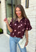 Classic polka dots meet rich fall color in this charming burgundy top! Featuring a soft mauve polka dot print, this top is an effortless way to add personality to your everyday wardrobe. The hidden button front creates a clean, polished look, while the foldover neckline and front pocket add timeless details you'll love. Finished with short puff sleeves, this versatile top is perfect for everything from workdays to weekend brunches and pairs beautifully with your favorite fall denim.