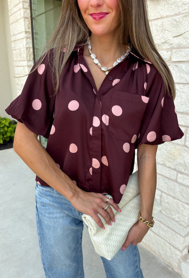 Classic polka dots meet rich fall color in this charming burgundy top! Featuring a soft mauve polka dot print, this top is an effortless way to add personality to your everyday wardrobe. The hidden button front creates a clean, polished look, while the foldover neckline and front pocket add timeless details you'll love. Finished with short puff sleeves, this versatile top is perfect for everything from workdays to weekend brunches and pairs beautifully with your favorite fall denim.
