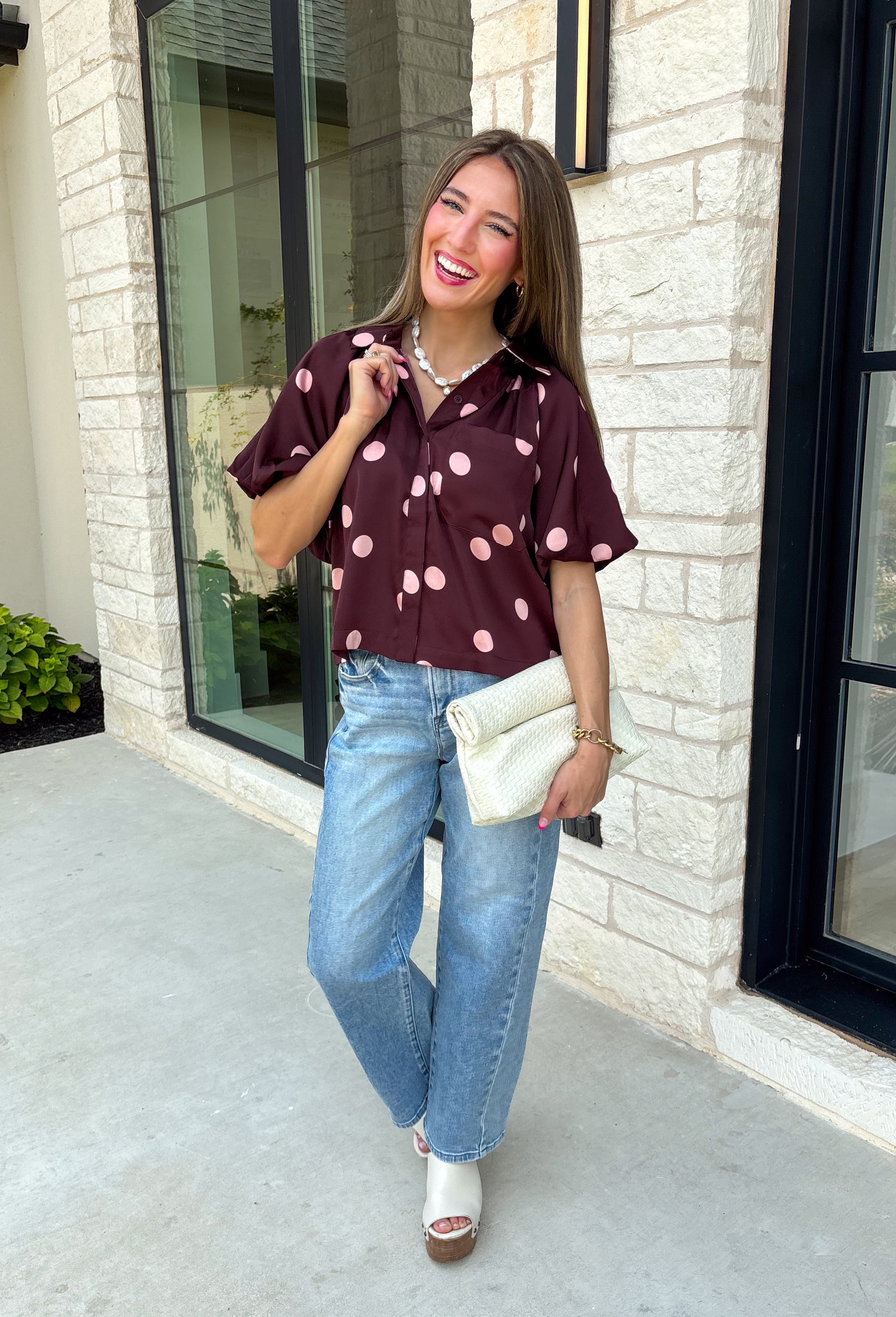 Classic polka dots meet rich fall color in this charming burgundy top! Featuring a soft mauve polka dot print, this top is an effortless way to add personality to your everyday wardrobe. The hidden button front creates a clean, polished look, while the foldover neckline and front pocket add timeless details you'll love. Finished with short puff sleeves, this versatile top is perfect for everything from workdays to weekend brunches and pairs beautifully with your favorite fall denim.